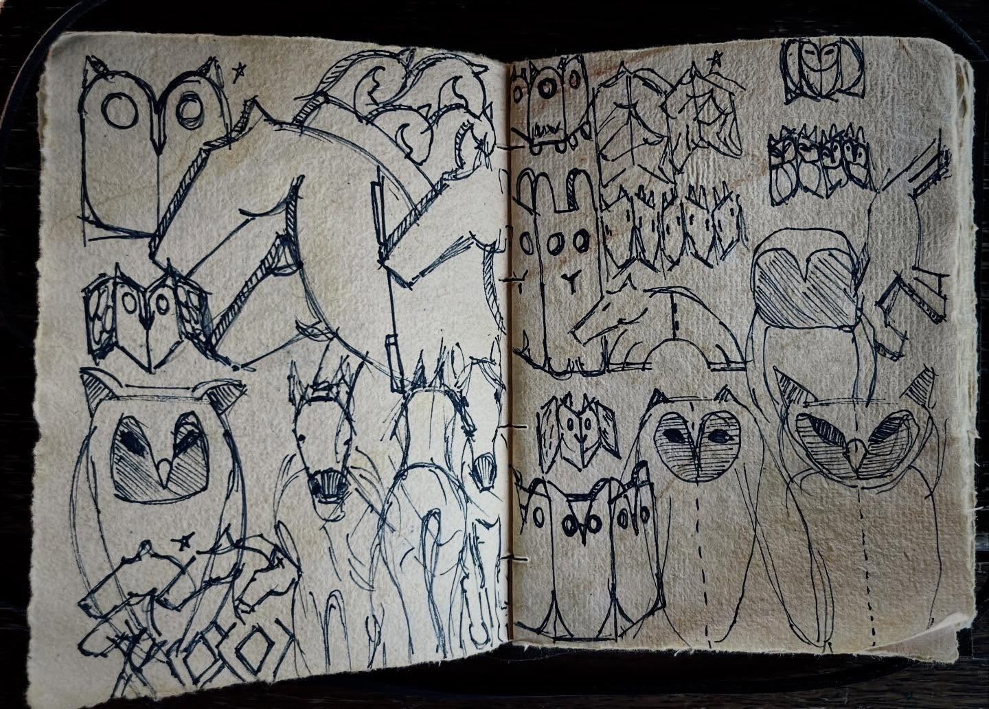 A sketchbook page filled with hand-drawn doodles of owls, foxes, wolves, and other animal faces, done with black ink on tan paper.