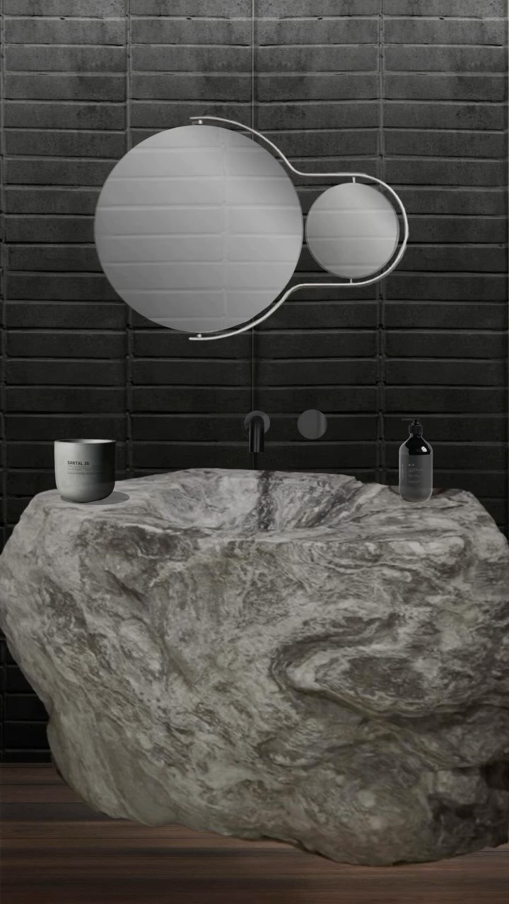 A bathroom with a large, natural stone vessel sink, a dark wall with horizontal lines, a round mirror with a smaller circle mirror, and a soap dispenser on the sink.