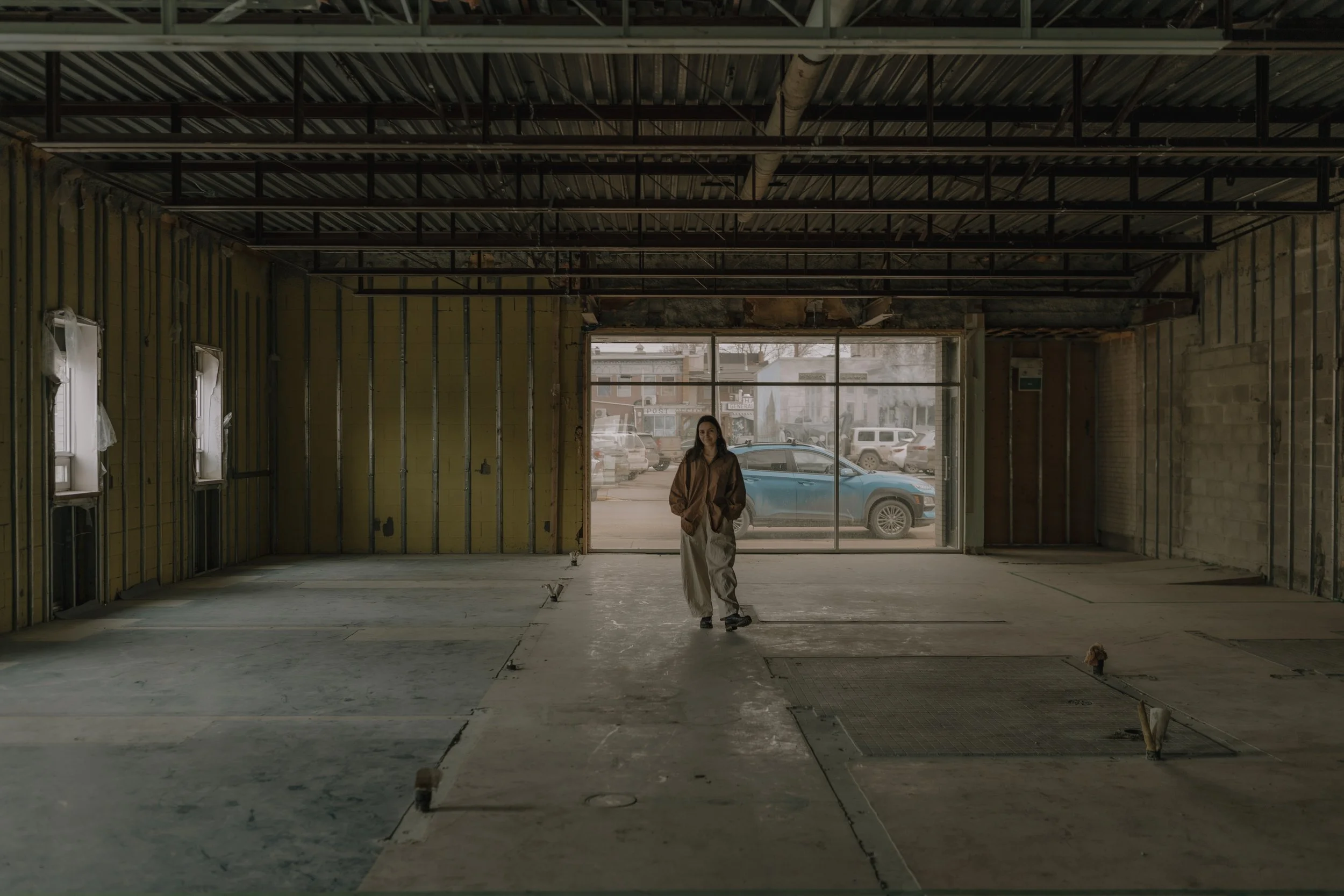 Person walks across concrete floor in empty Spa Building in Lacombe construction site, with yellow walls, beams, and large windows.