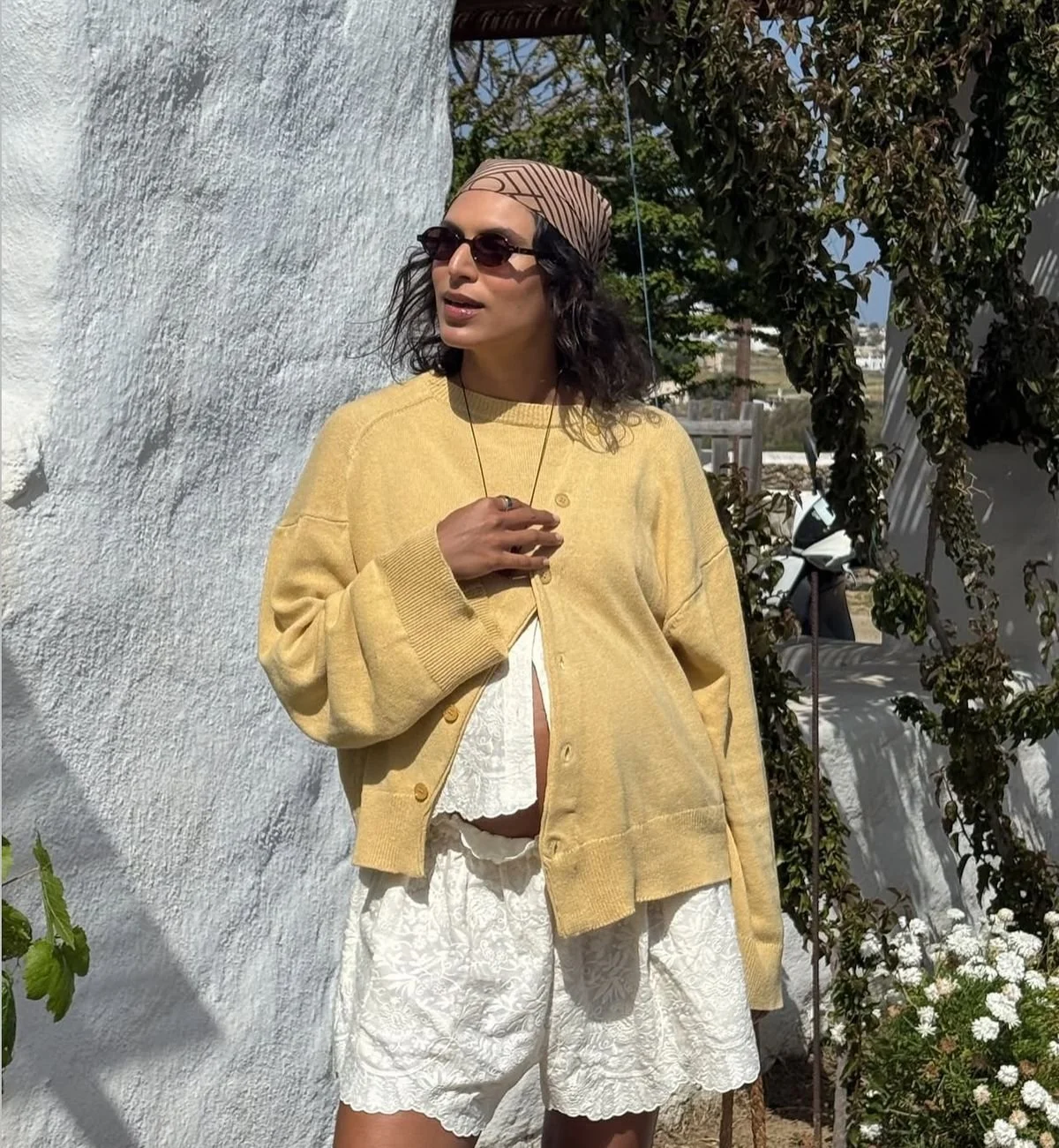 Pregnant woman models Bohème Goods The Asymmetric Knit open wheat cardigan with flared sleeves and lace shorts in sunlit outdoor setting.