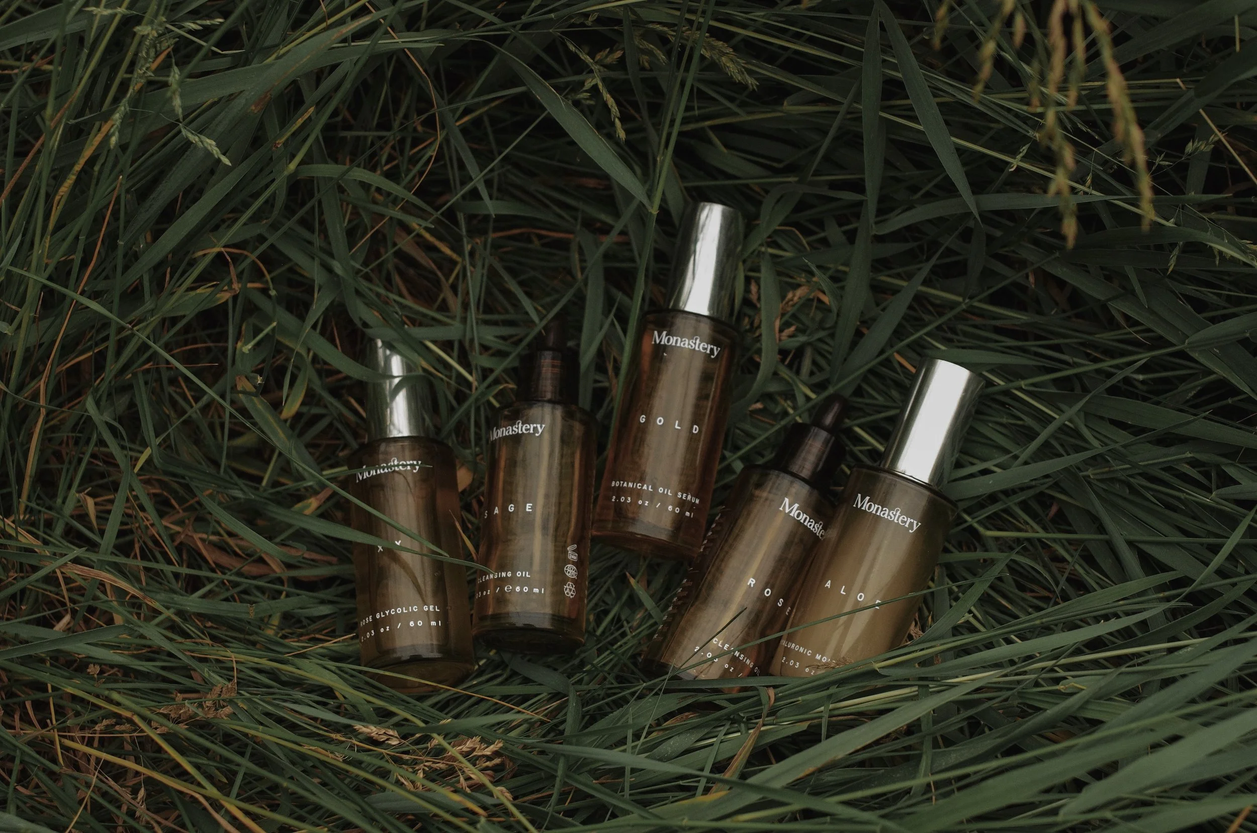 Amber glass bottles from Monastery Made natural skincare nestled among tall green reeds and grass, ideal to shop sustainable skincare.