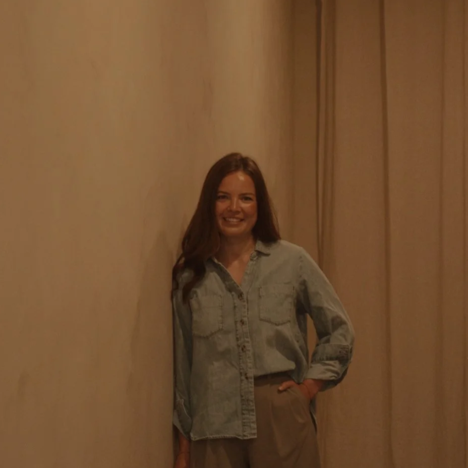 Japanese headspa specialist Carmen leans against spa wall smiling at camera in denim shirt