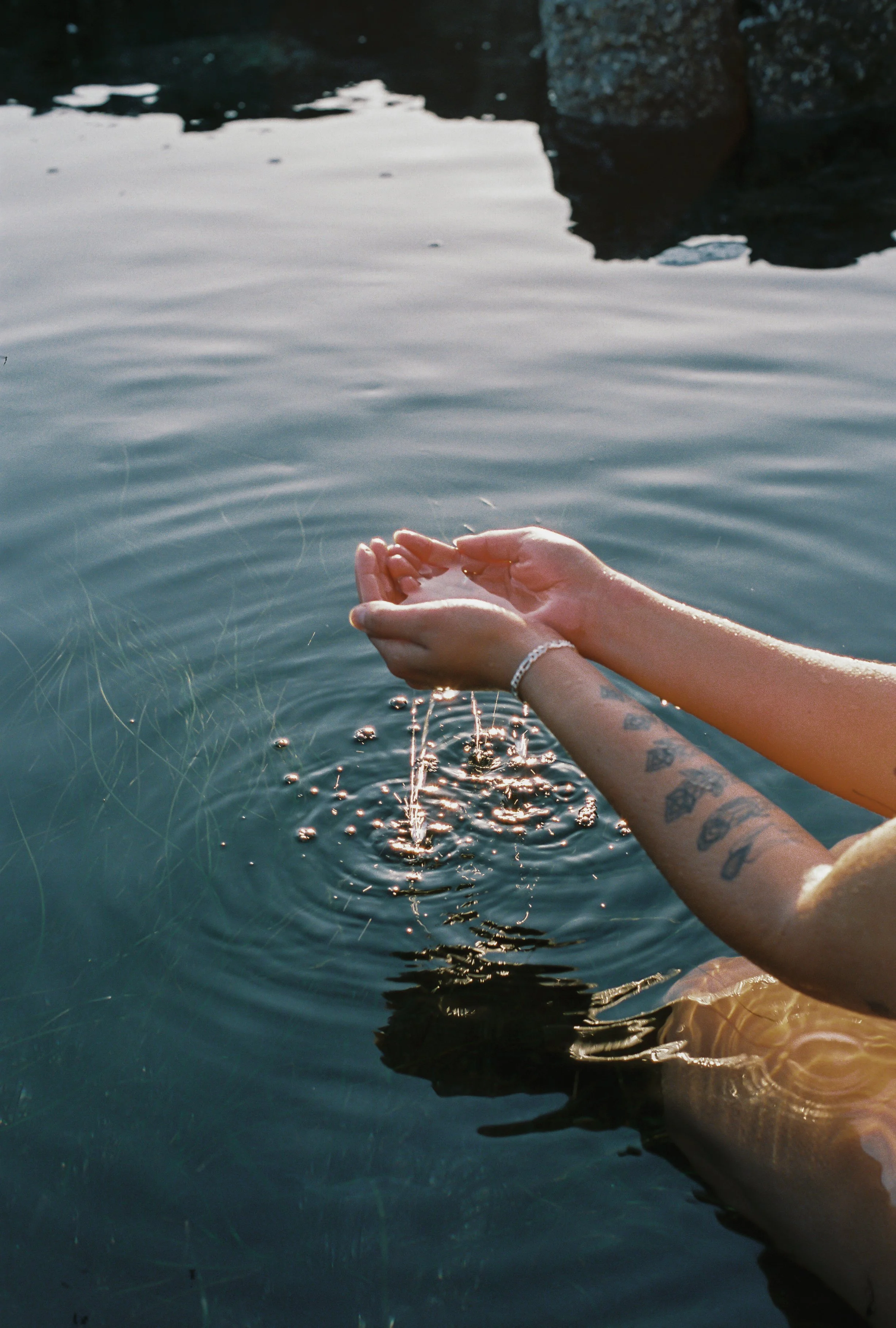 Serene view of hands holding dripping water in Tofino ocean pool, embodying offering sustainable skincare and facials.
