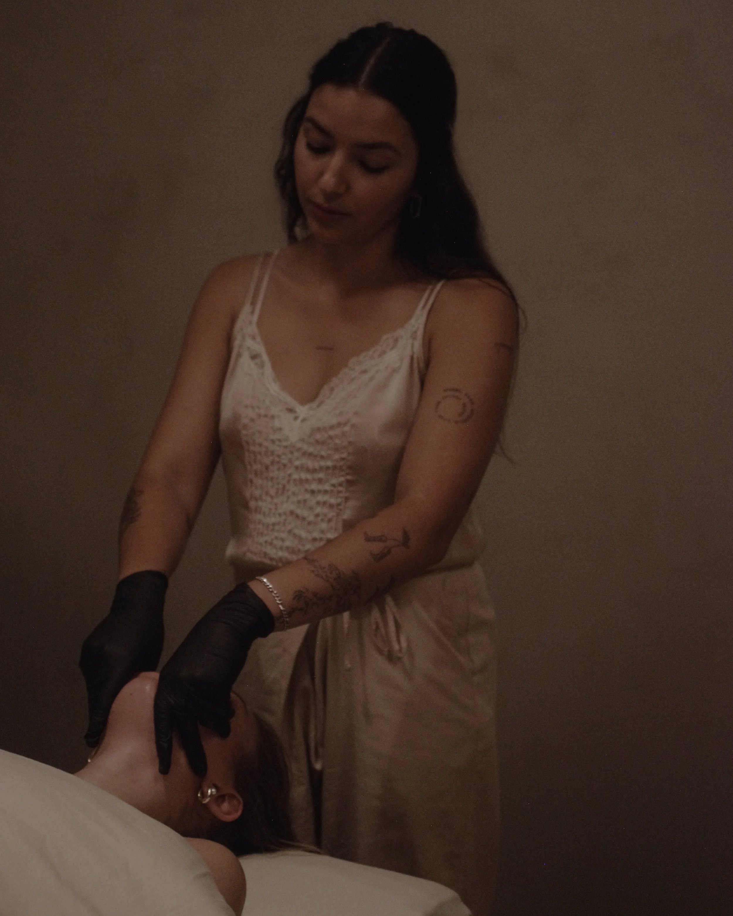 Women stand above client performing buccal massage with black gloves in spa in central Alberta