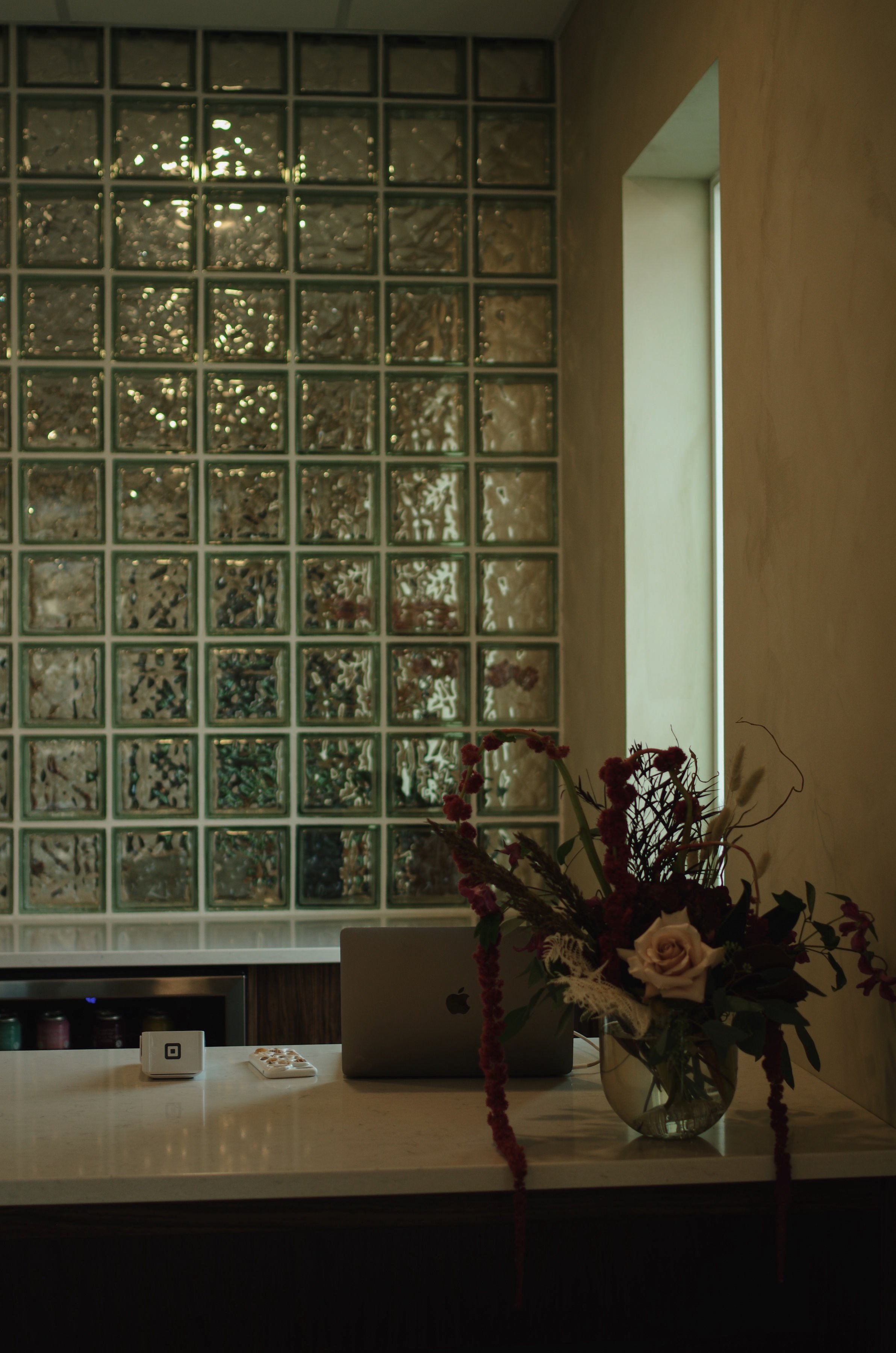 Front desk at Unique Spa in Lacombe with glowing glass block wall, vase of pink roses and red berries, MacBook, and wabi-sabi vibe.