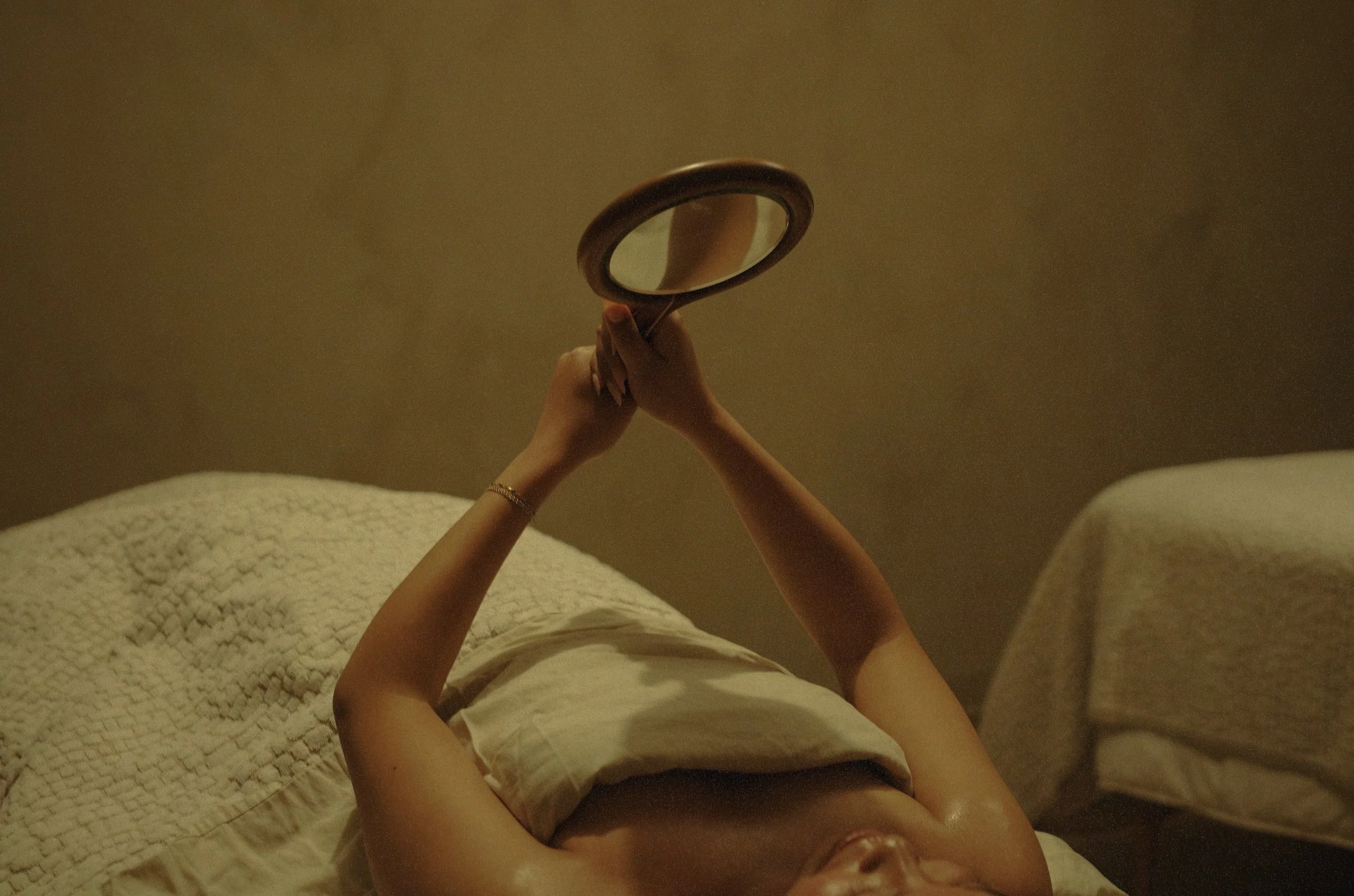 Woman melting stress away in spa in Lacombe reclines on bed, holding mirror to admire her glowing post-facial skin.