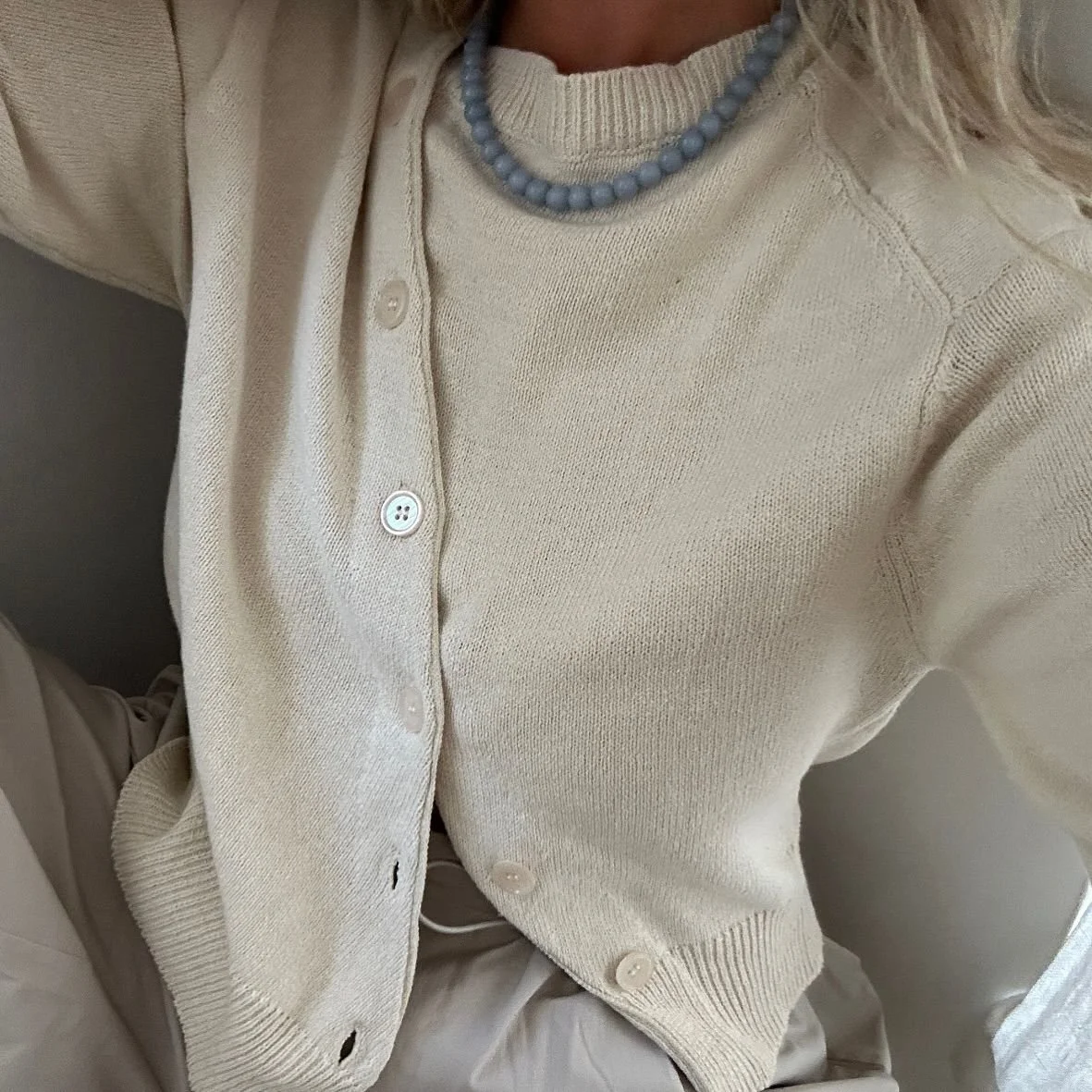 Sarah wearing Bohème Goods The Asymmetric Knit Akoya cardigan with wide sleeves and blue beaded necklace, posed sitting