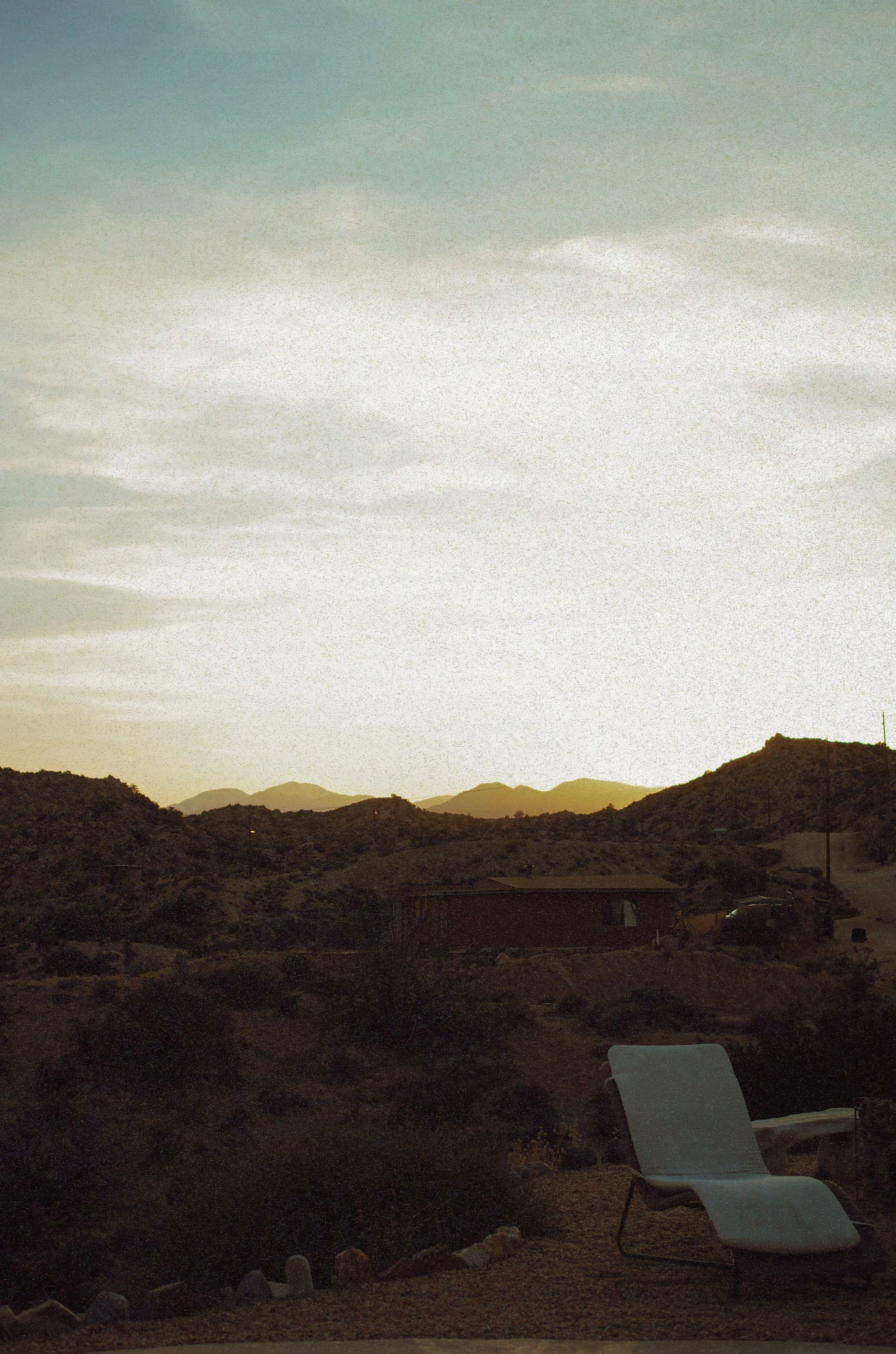 Serene desert landscape at sunset with a white lounge chair on gravel overlooking rocky hills, perfect for booking online hypnotherapy.