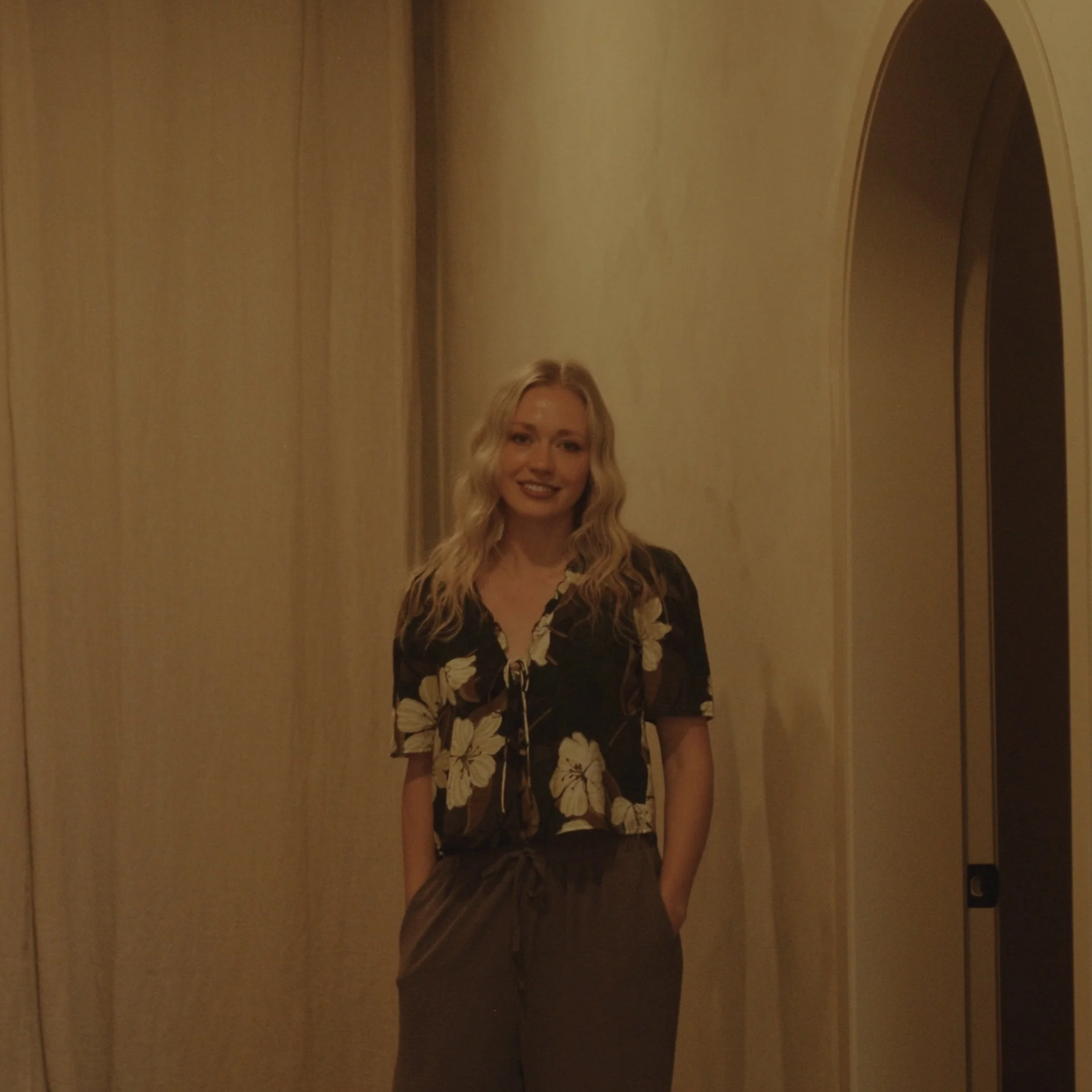 Teegan smile technician standing next to arched door way in floral shirt smiling at camera in Lacombe spa