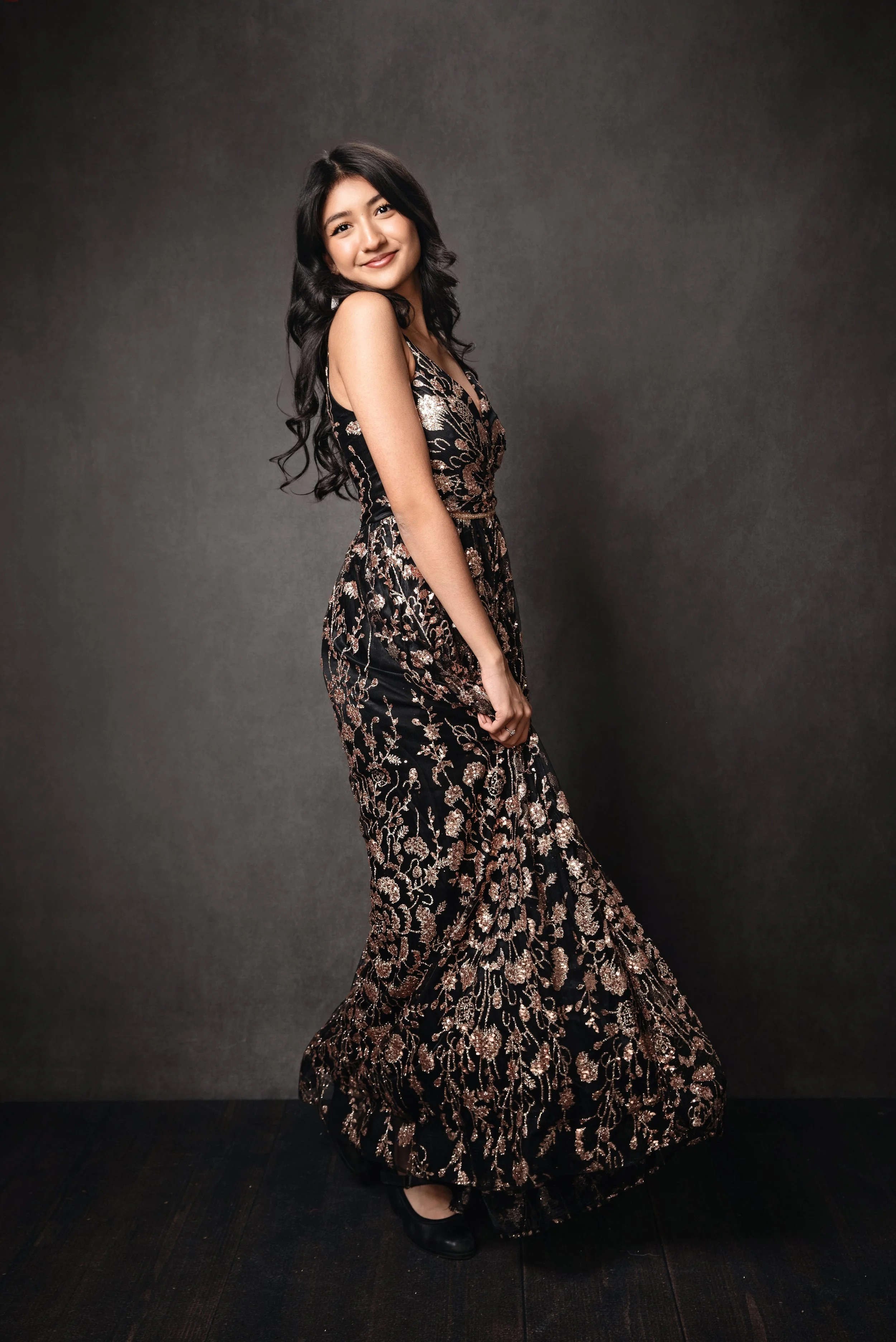 Professional branding portrait of a woman in a satin gray button-up blouse, sitting at a desk with a laptop, glasses in hand, and pink roses nearby during a lifestyle headshot session in San Antonio
