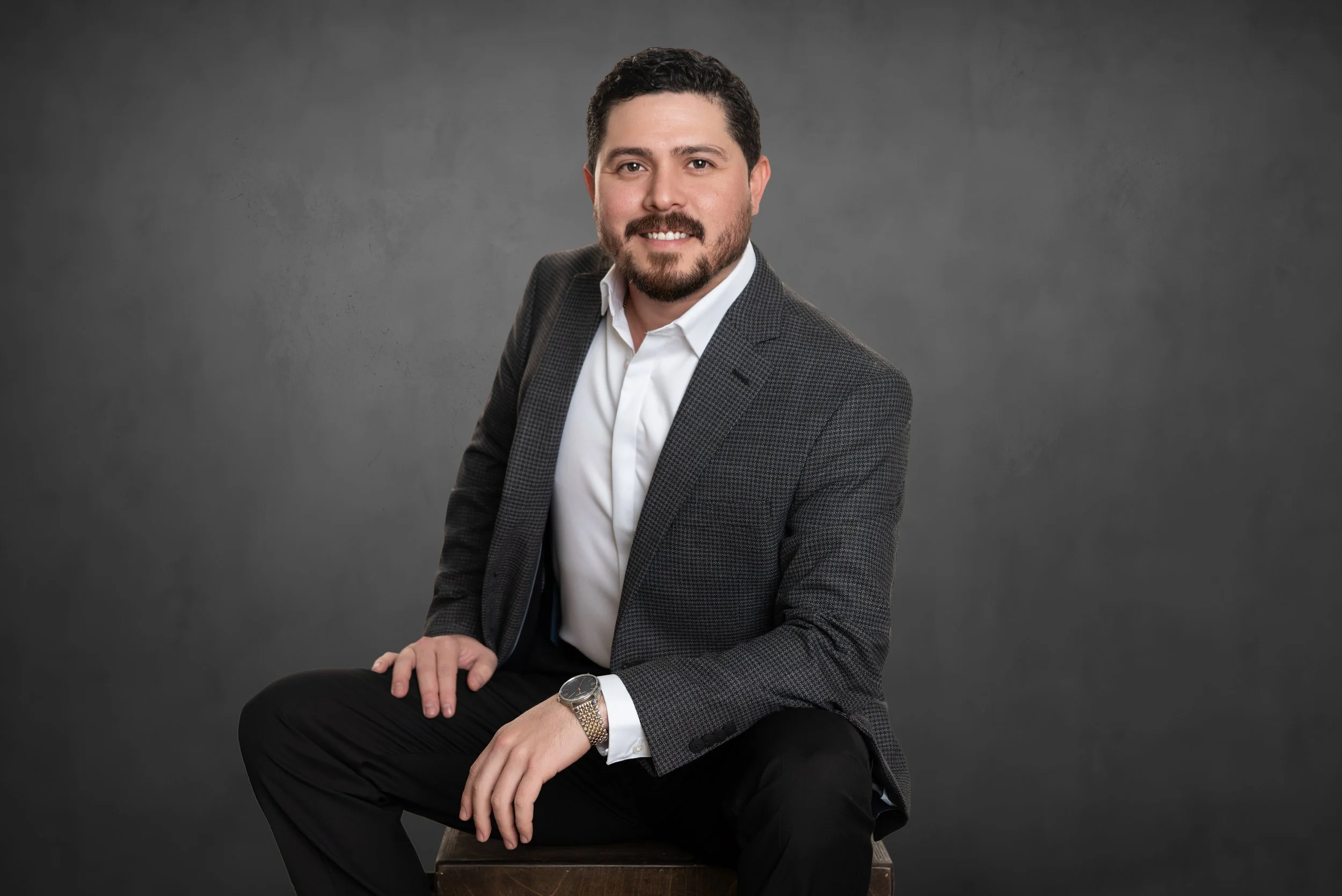 Professional men's headshot photo shoot in San Antonio TX showing a State Farm agent in a gray jacket sitting confidently against a studio background.