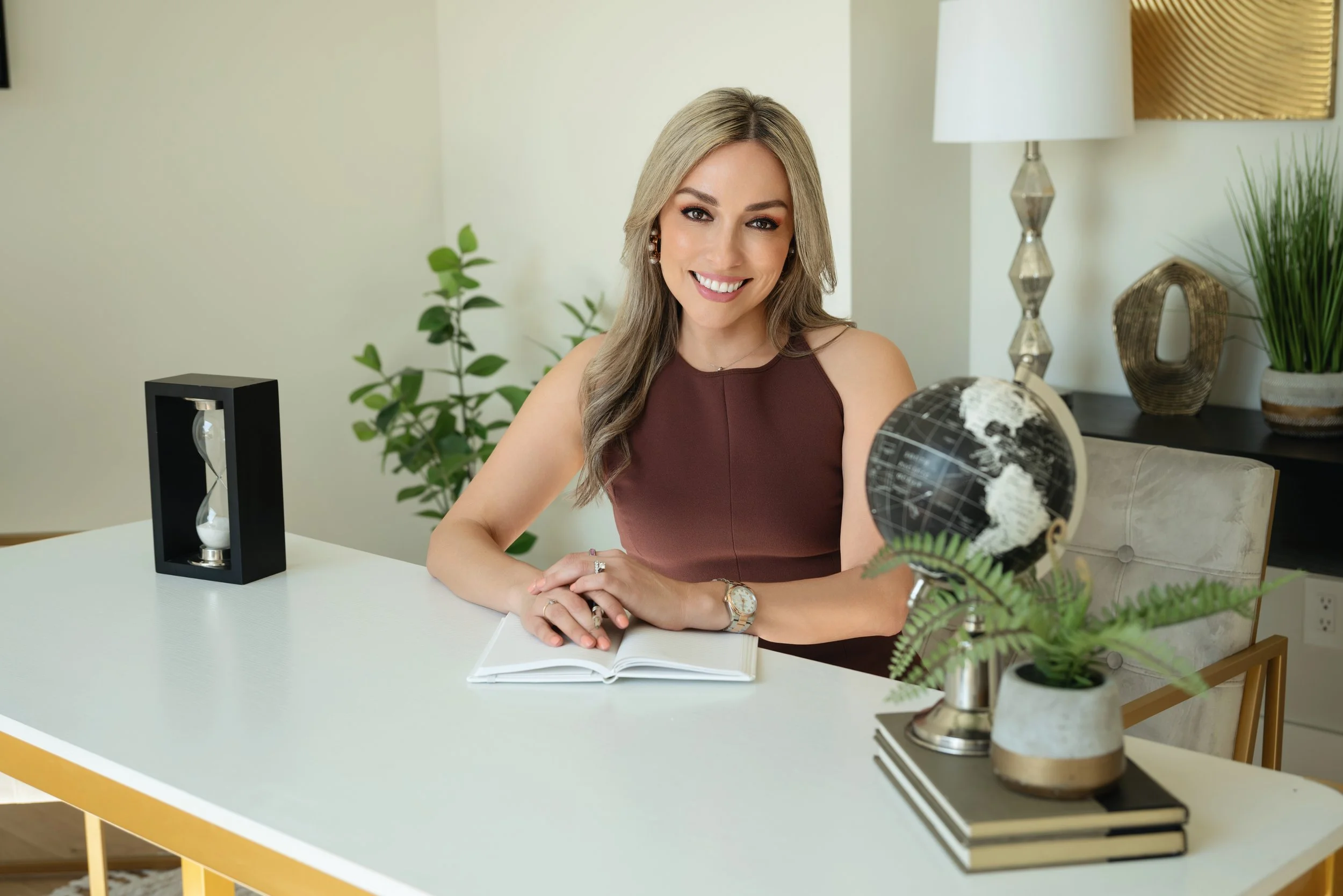 Husband and wife realtor team smiling together in a modern kitchen, with the woman leaning on the island in a red and white striped blouse and the man standing beside her in a blue blazer during a branding photo session in San Antonio