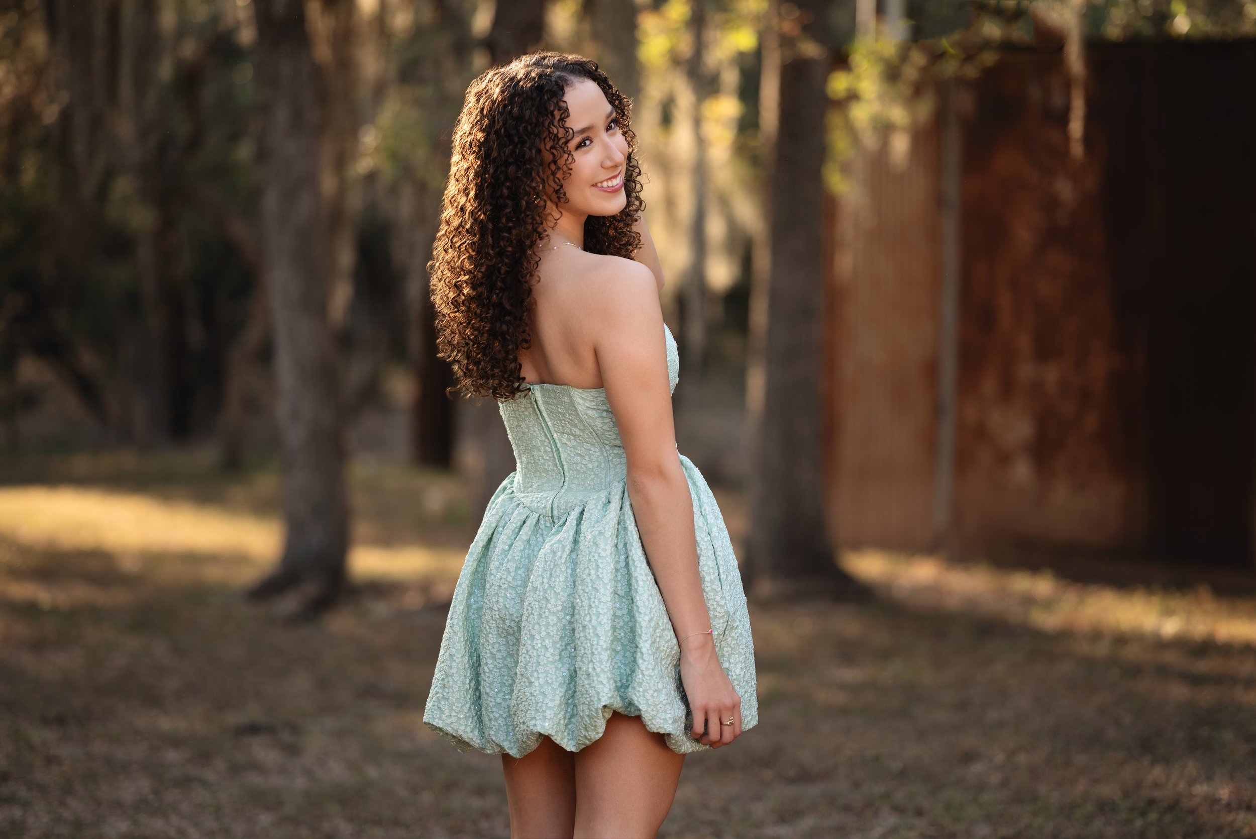Curly-haired senior looks over her shoulder during a session in Bracken Village.