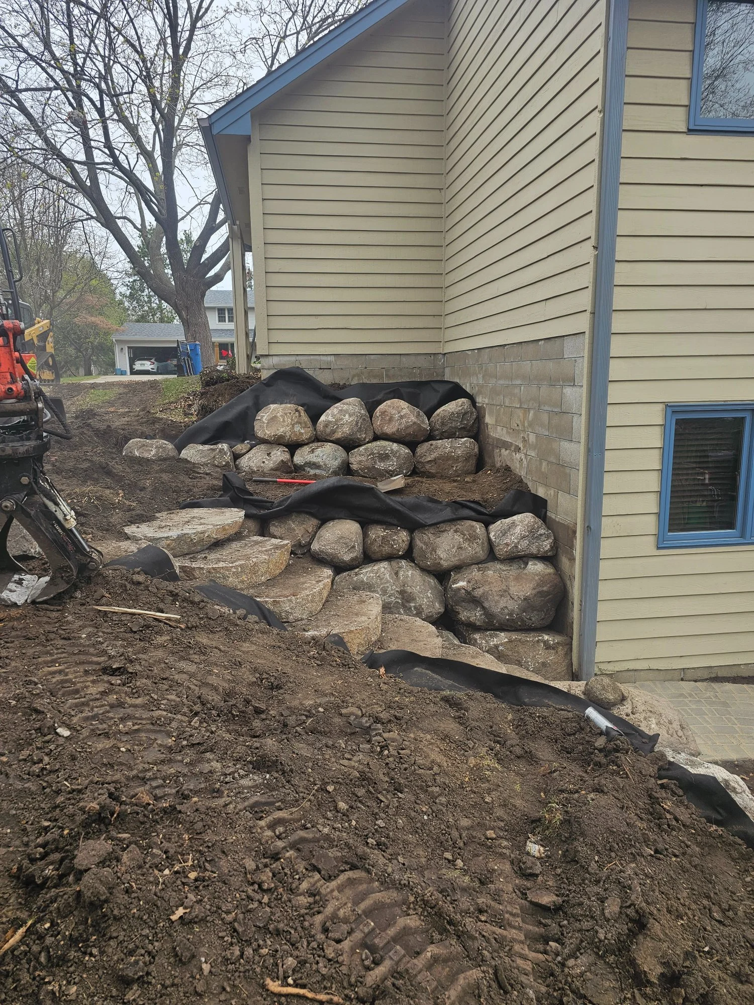 CMP grapple placing fieldstone boulders on Burnsville MN retaining wall — Heritage Outdoors excavator