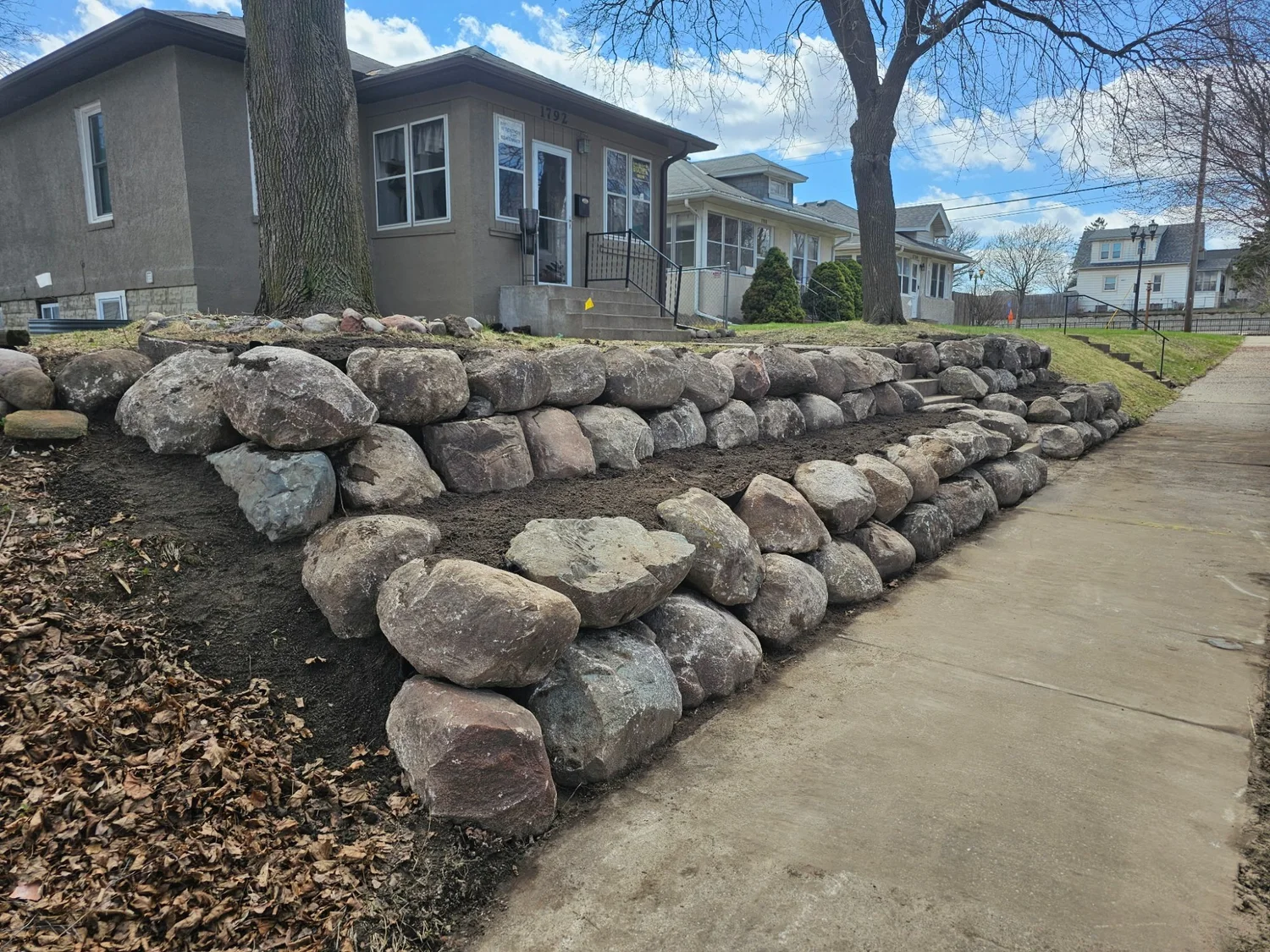Street view of completed tiered boulder wall across full front yard — Maplewood MN — Heritage Outdoors