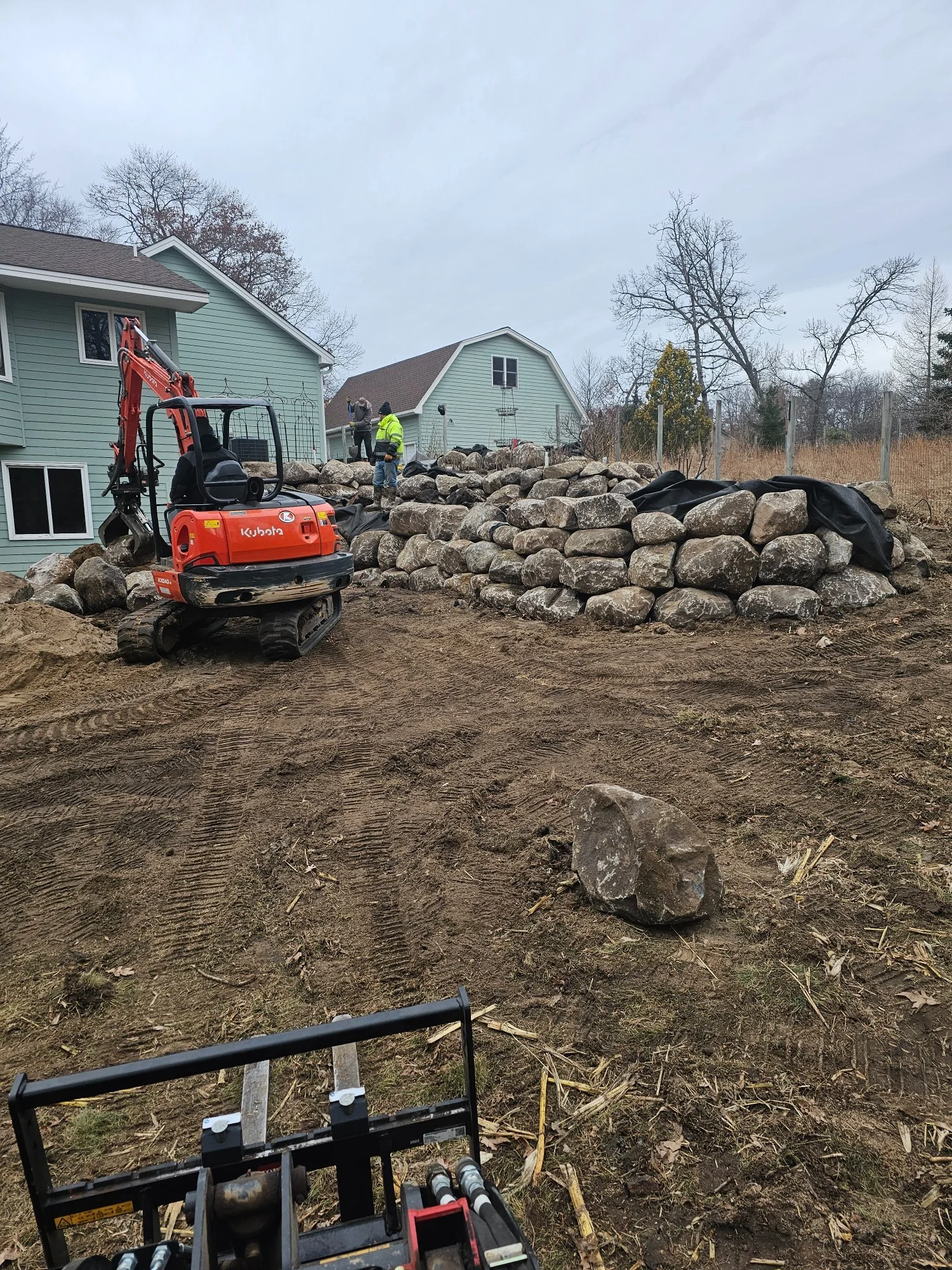 Fieldstone boulder wall installation in progress — Wyoming MN — Heritage Outdoors crew and Kubota excavator
