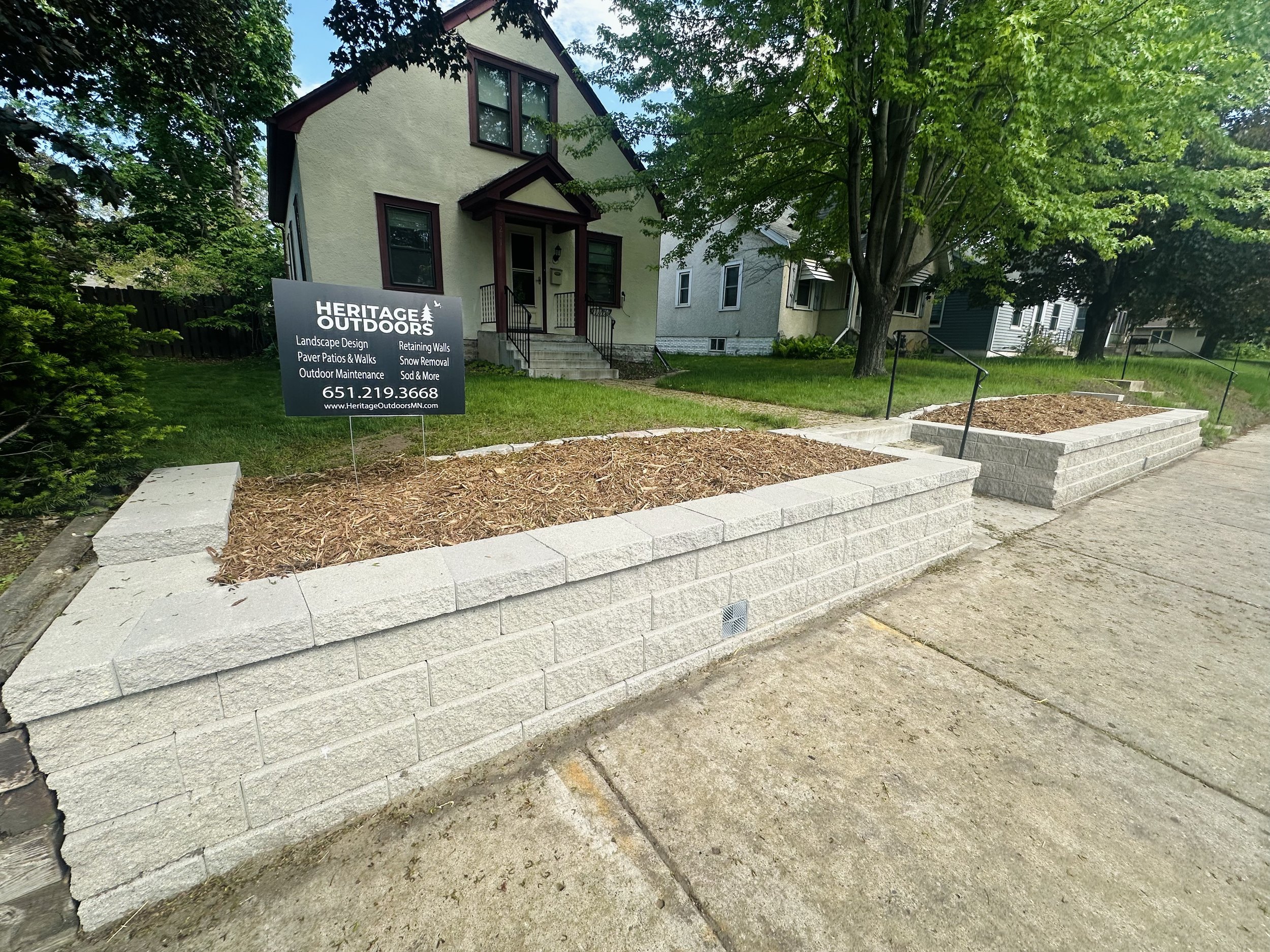 Completed Versa-Lok Granite Gray retaining wall with mulch garden beds and Heritage Outdoors yard sign — Minnehaha, Minneapolis MN — 2024