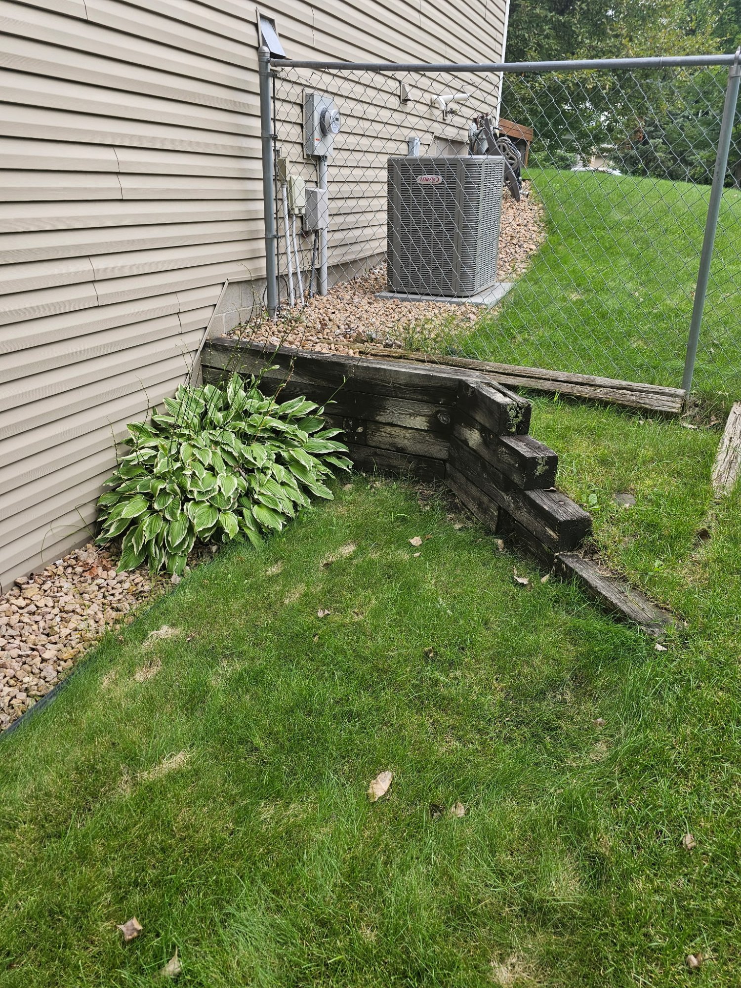 Failing timber retaining wall bowing away from house in Centerville MN — before boulder wall installation by Heritage Outdoors