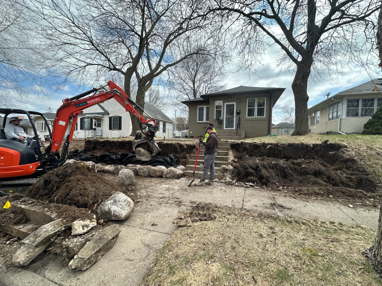 CMP grapple placing boulder on retaining wall — Maplewood MN — Heritage Outdoors excavator operator