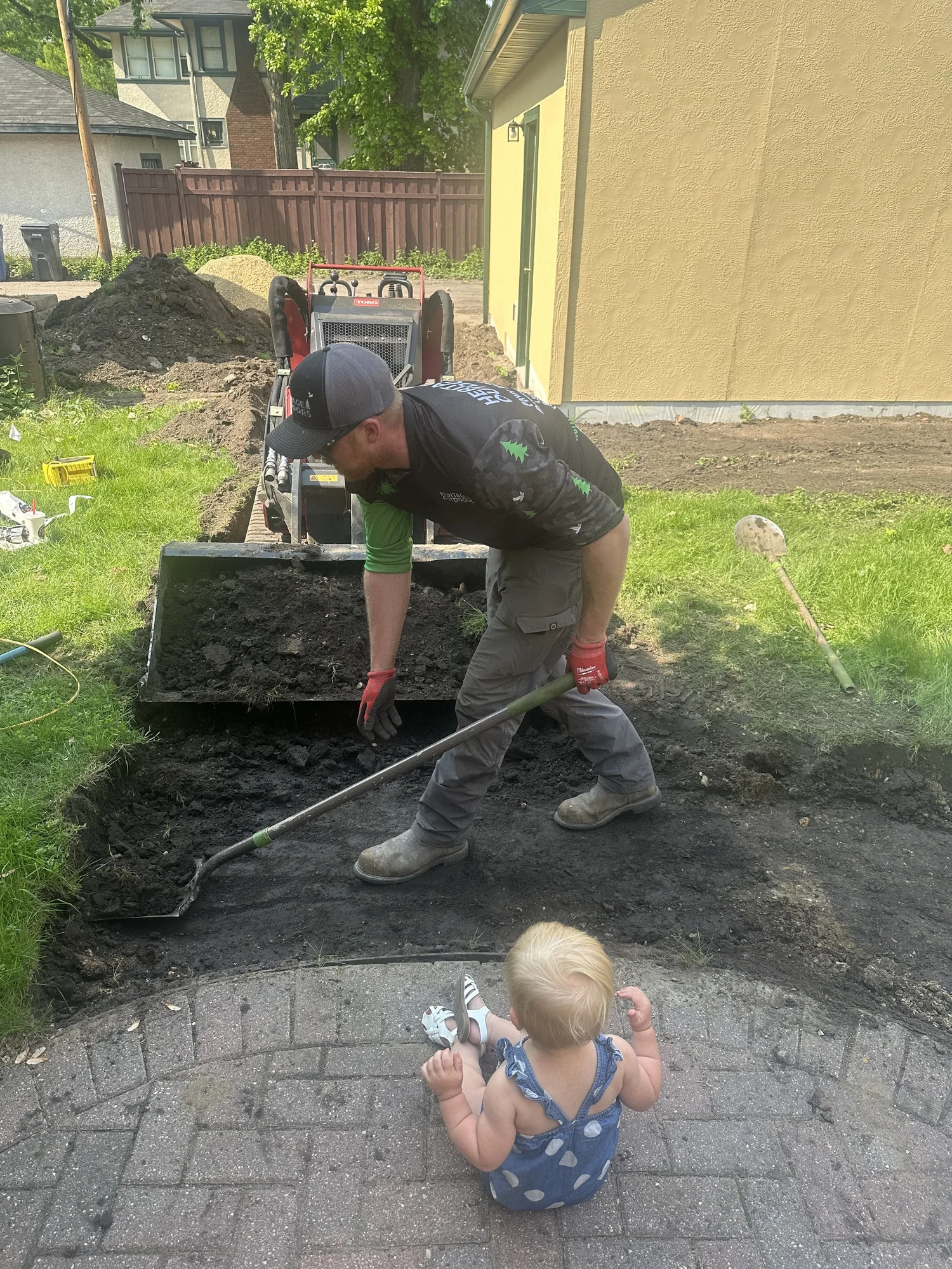 Jacob hand-grading walkway base with daughter supervising from existing patio — Mac-Groveland Saint Paul MN — Heritage Outdoors 2025