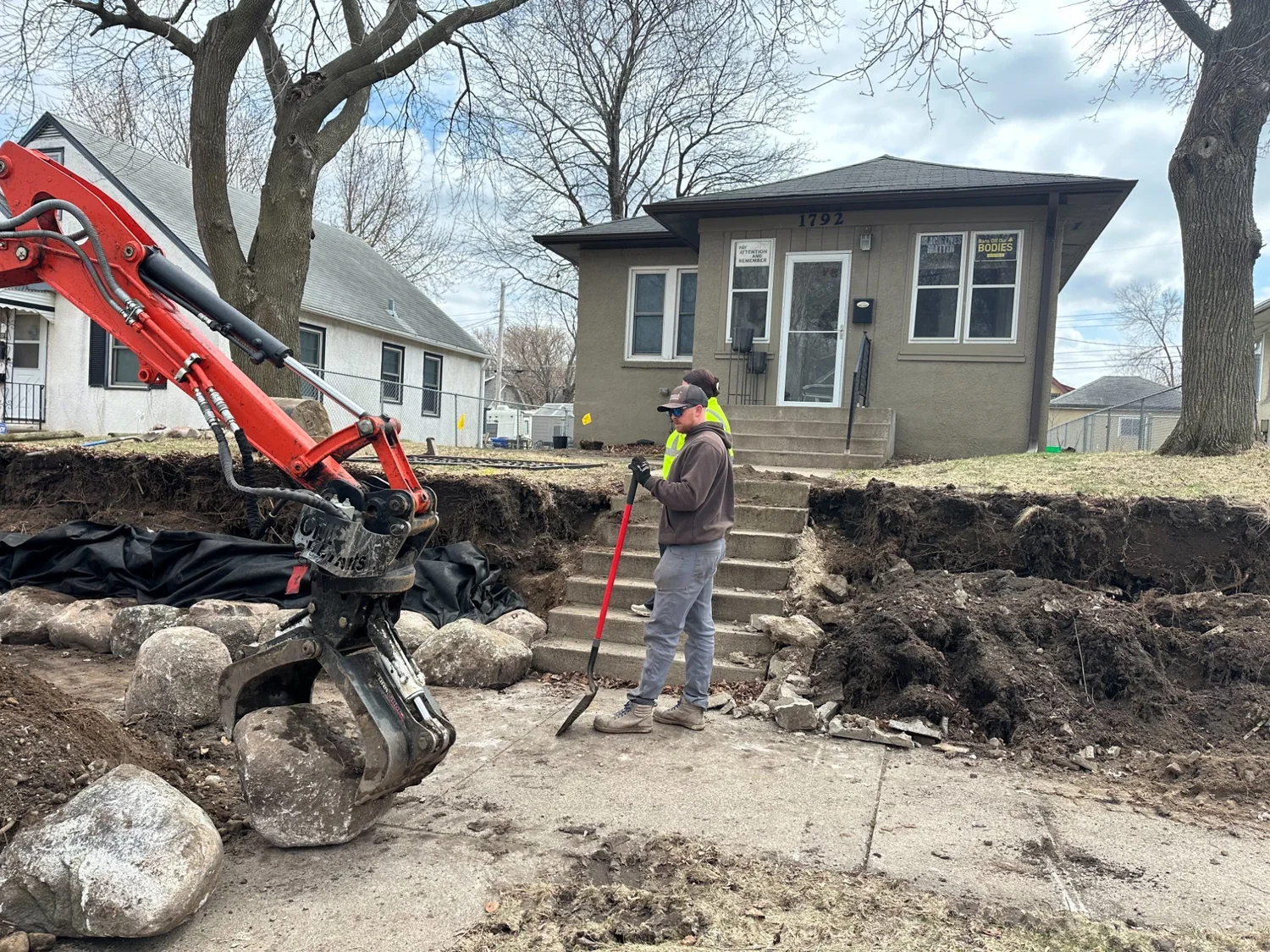 Kubota excavator placing fieldstone boulders — Maplewood MN front yard — Heritage Outdoors