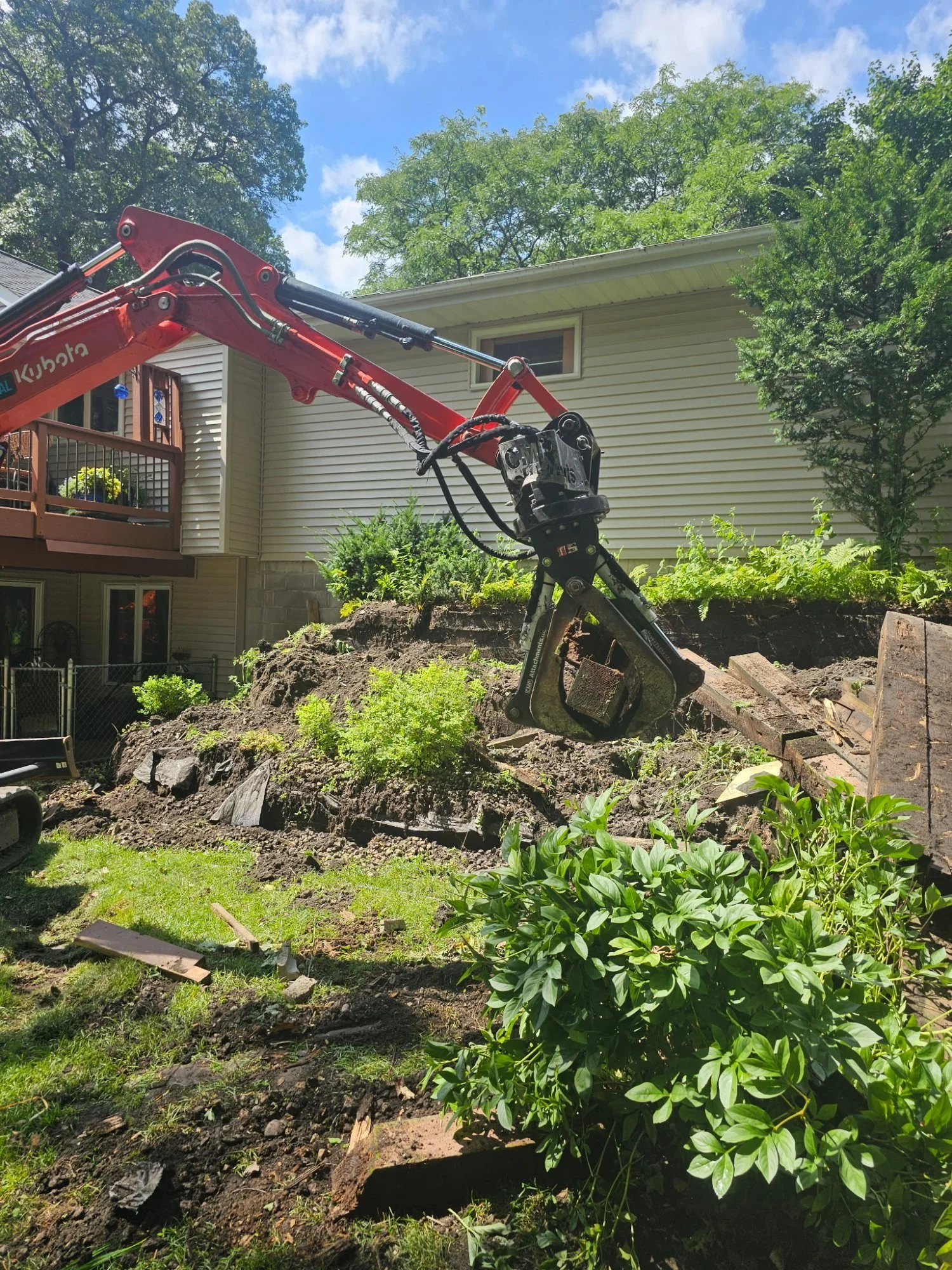 Kubota mini excavator with CMP grapple demolishing timber retaining wall — Woodbury MN — Heritage Outdoors 2025