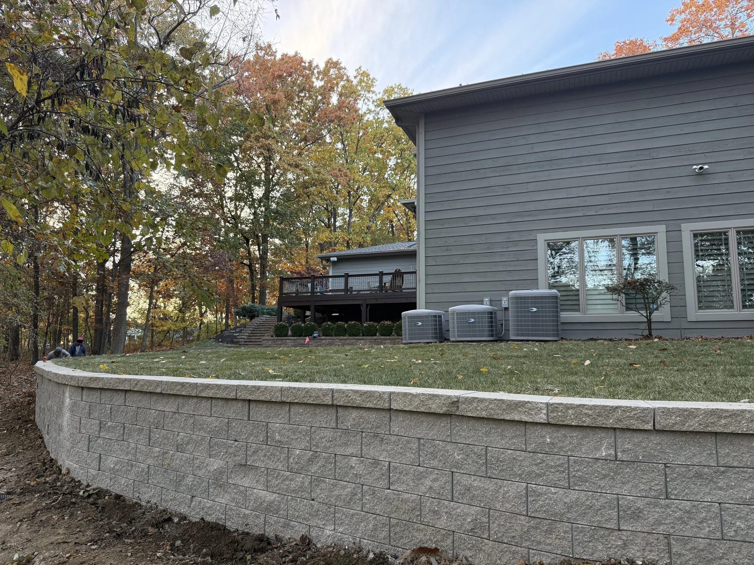 Backyard with a raised wooden deck, house with horizontal siding, and fallen leaves among the trees in autumn.
