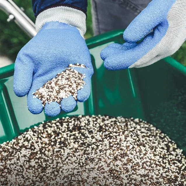 Person wearing blue gloves holding small white and black pebbles over a green container filled with similar pebbles.