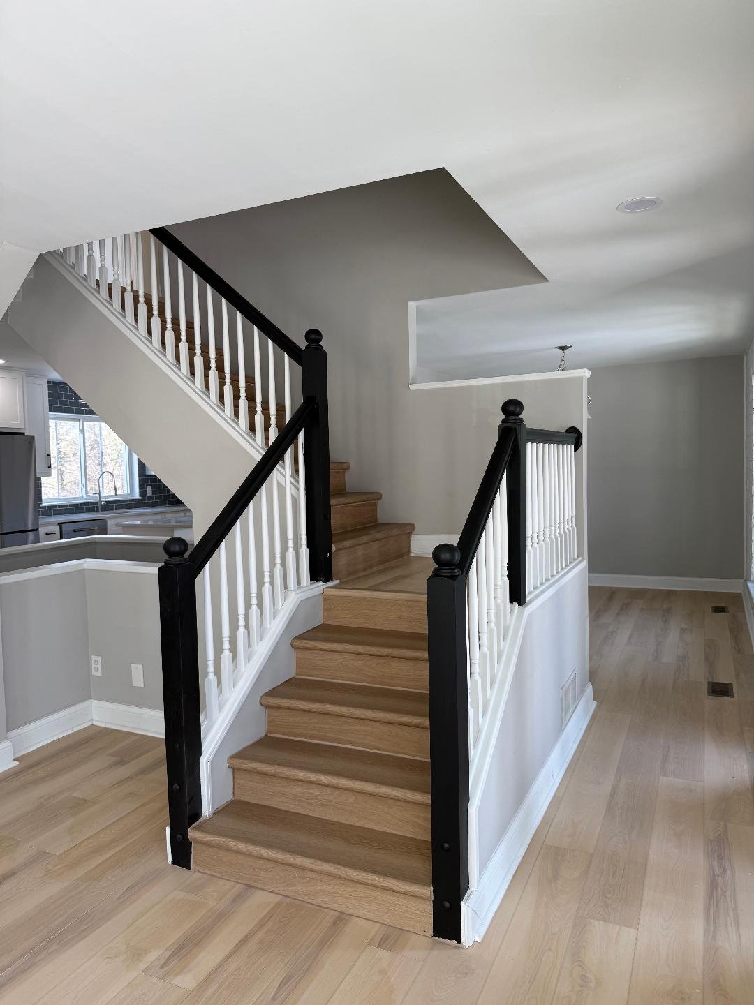 Interior of a house featuring a staircase with wooden steps, black and white railing, and light wooden flooring.