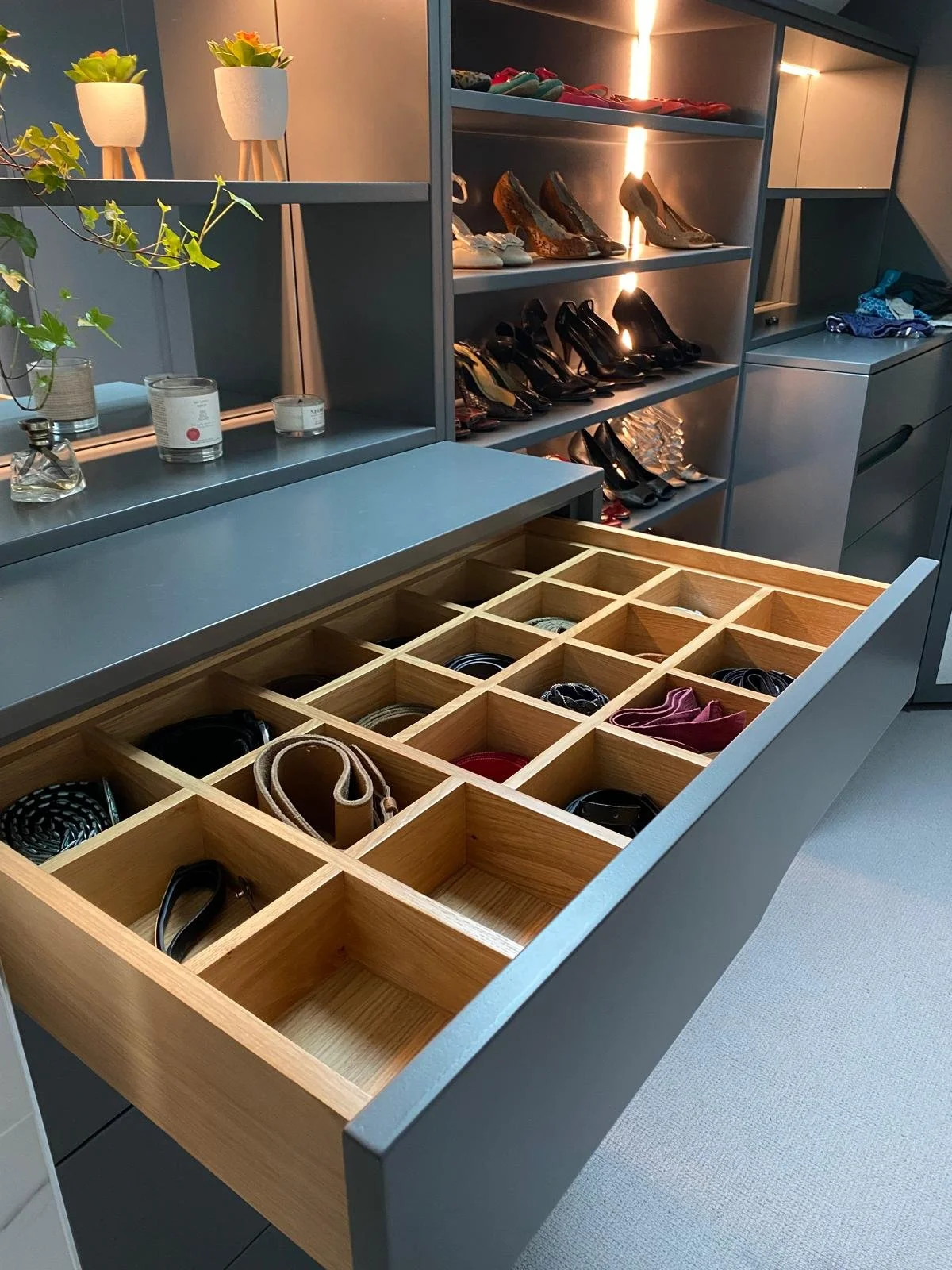 An open drawer in a dressing room showing solid wood drawer divider for belts. The is also a shoe rack which is lit with LED strips. The cabinetry is spray painted in a dark bluey green colour.