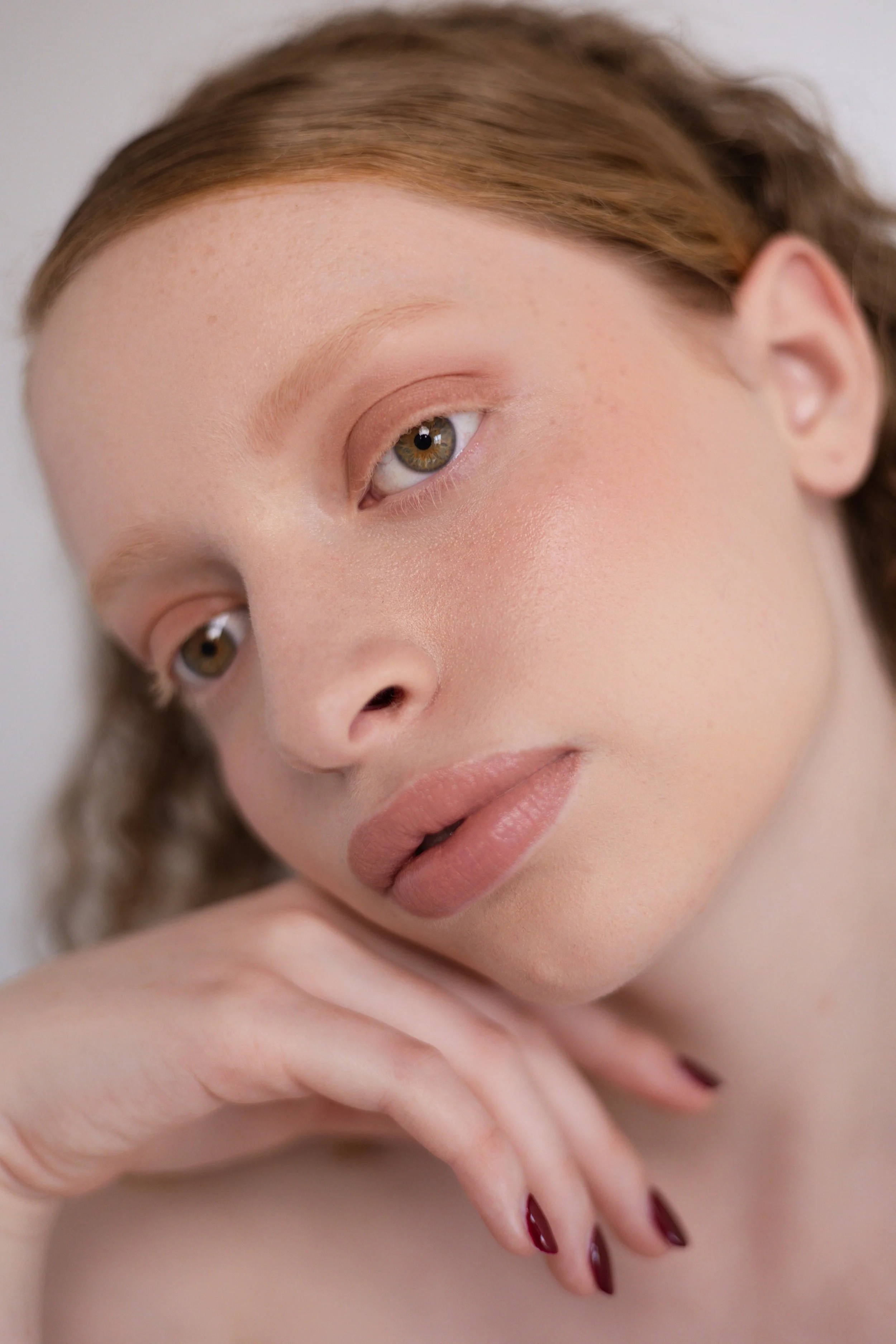 Shooting beauté. Portrait d'une jeune femme aux cheveux auburn, avec maquillage naturel et peau claire, posant avec sa main sous son menton.