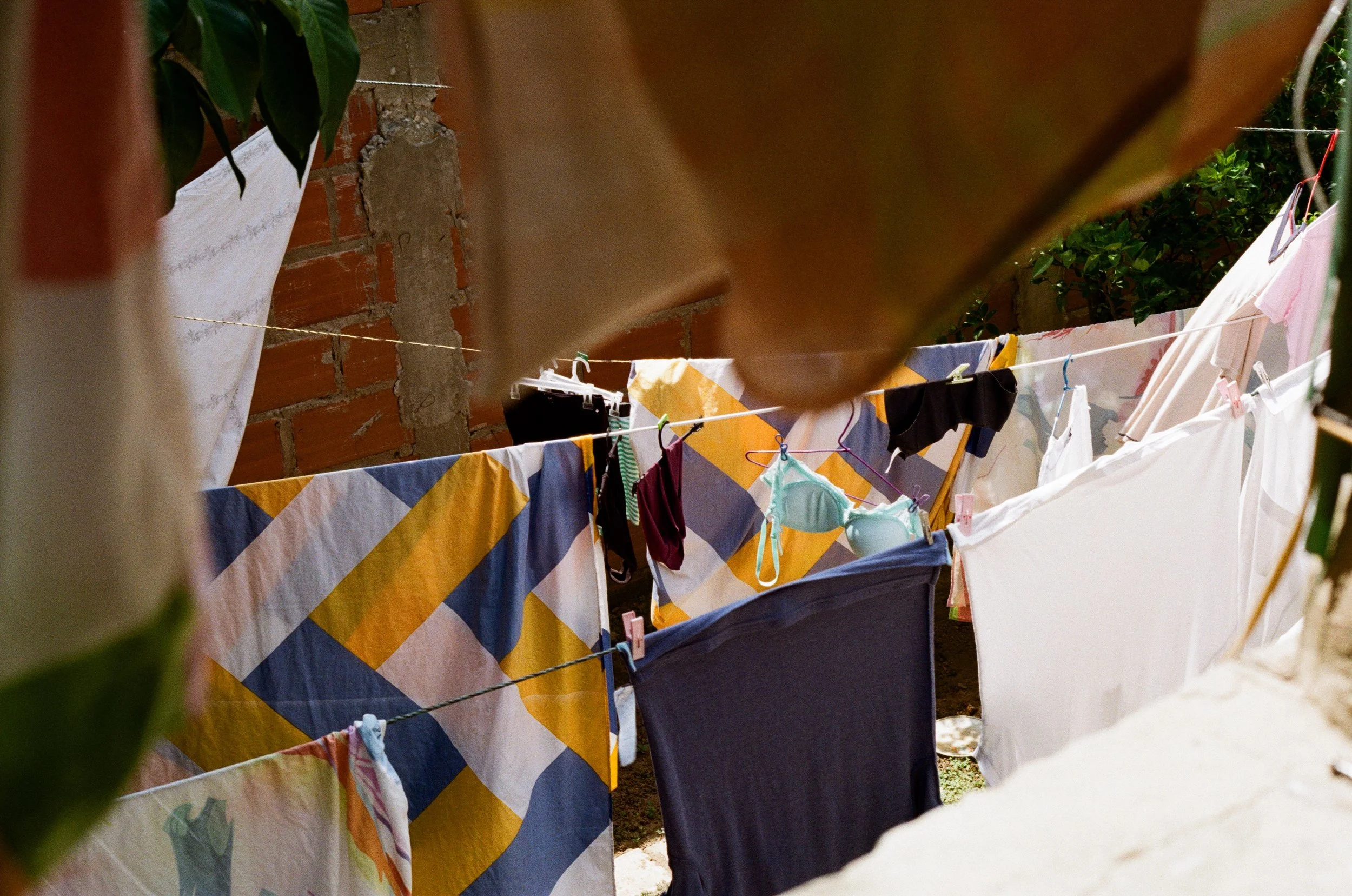 Linge à sécher suspendu sur une corde dans un jardin, avec un mur en briques et quelques plantes en arrière-plan.
