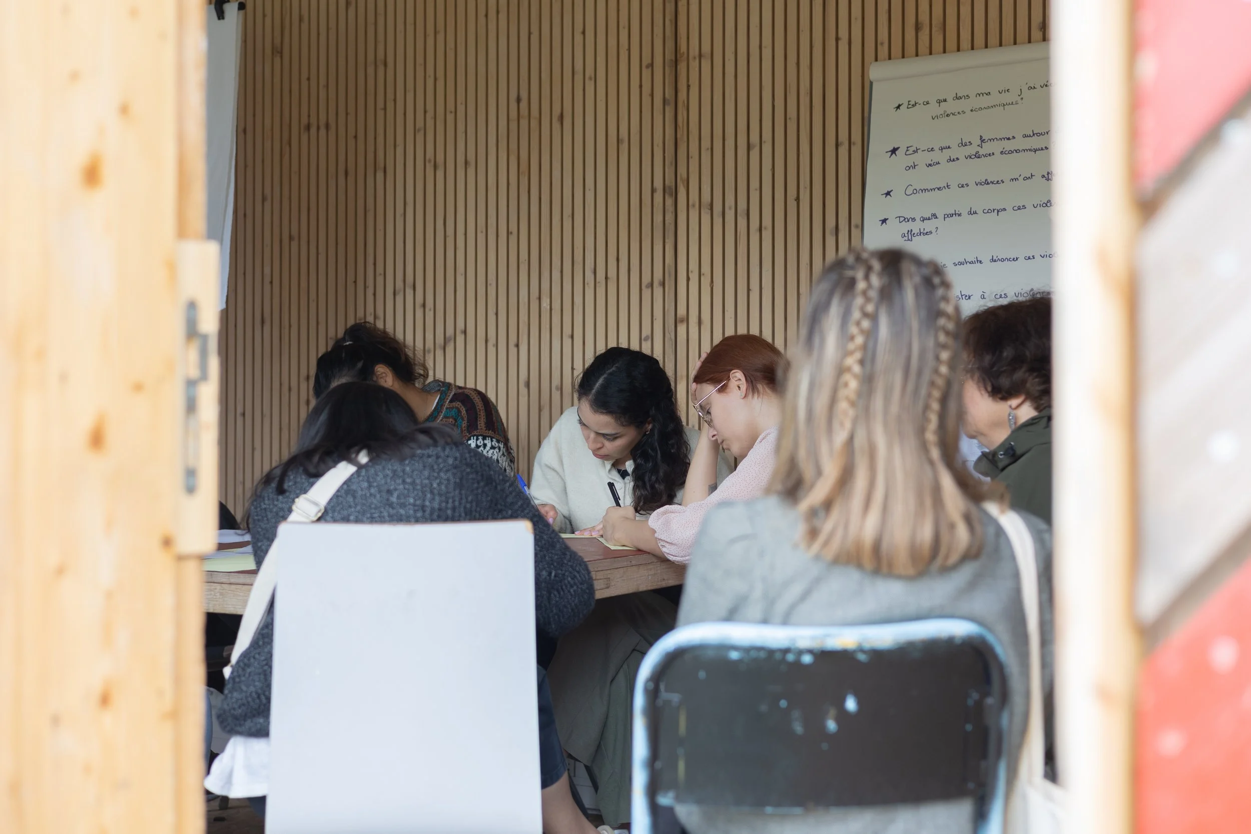 Groupe de femmes assises autour d'une table, concentrées, dans une salle en bois, avec un tableau blanc à l'arrière.