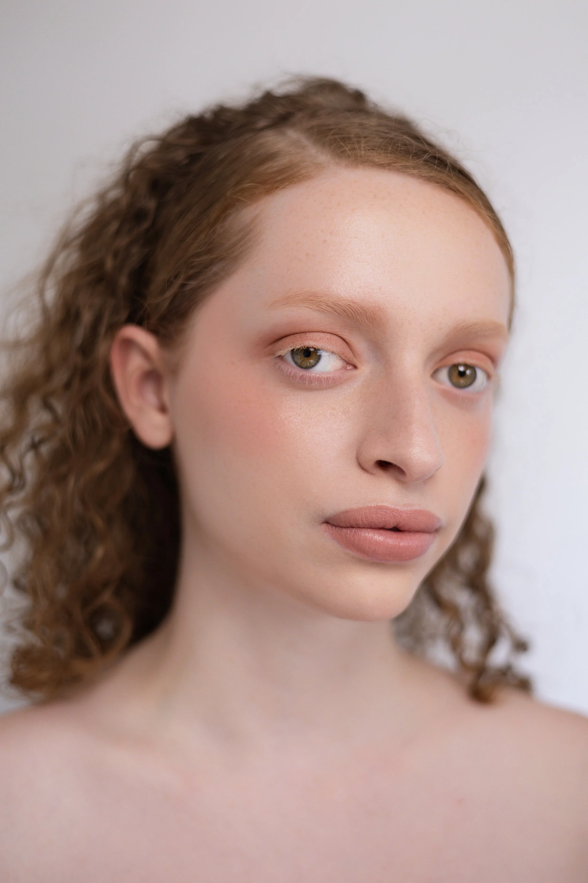 Shooting beauté. Jeune femme avec des cheveux roux bouclés, visage clair, maquillage naturel, regard doux et lèvres neutres.