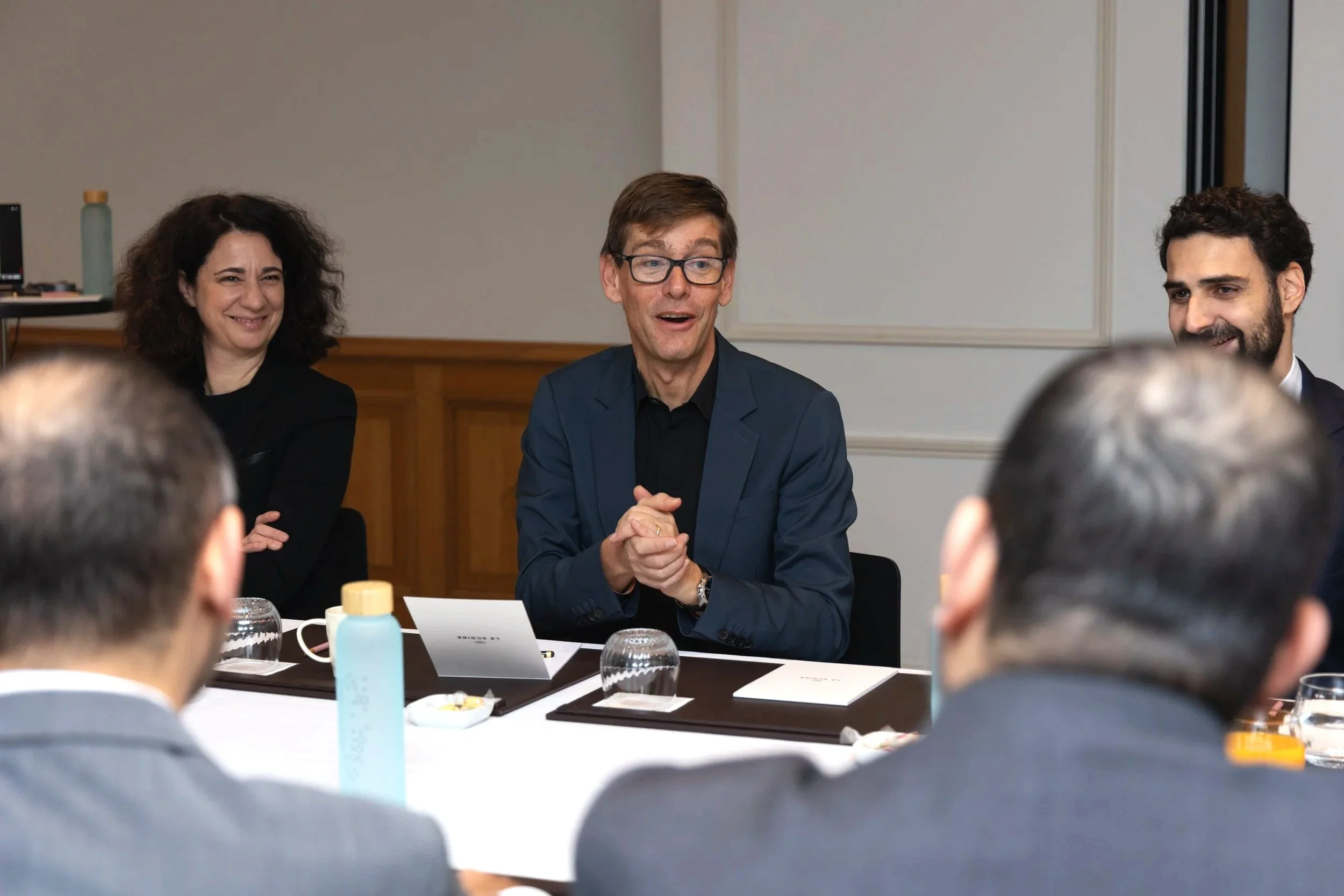 Un groupe de personnes lors d'une réunion, deux femmes et un homme assis à une table, en discussion et en train de sourire.