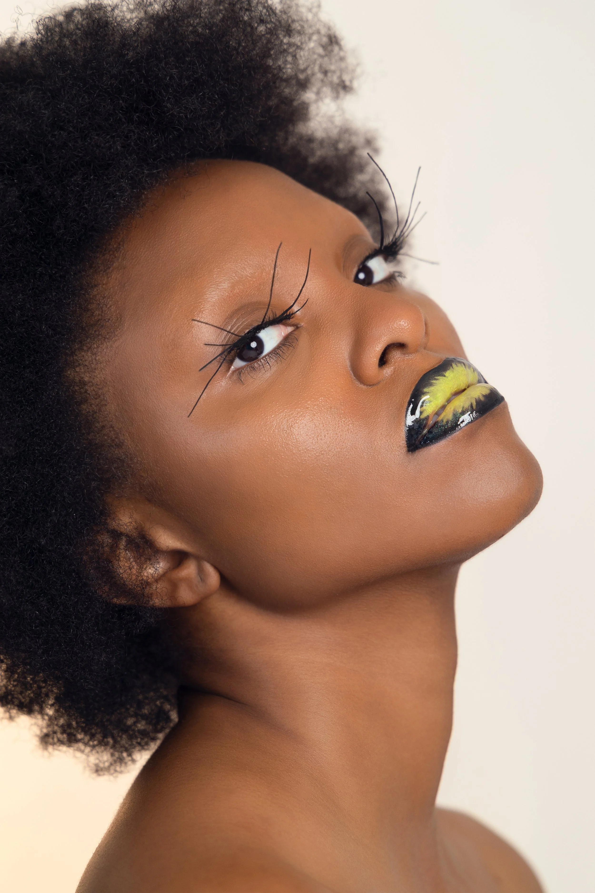 Shooting beauté. Portrait d'une femme noire avec un maquillage artistique, comprenant des lèvres jaunes et noires et des cils longs avec des extensions très voyantes.
