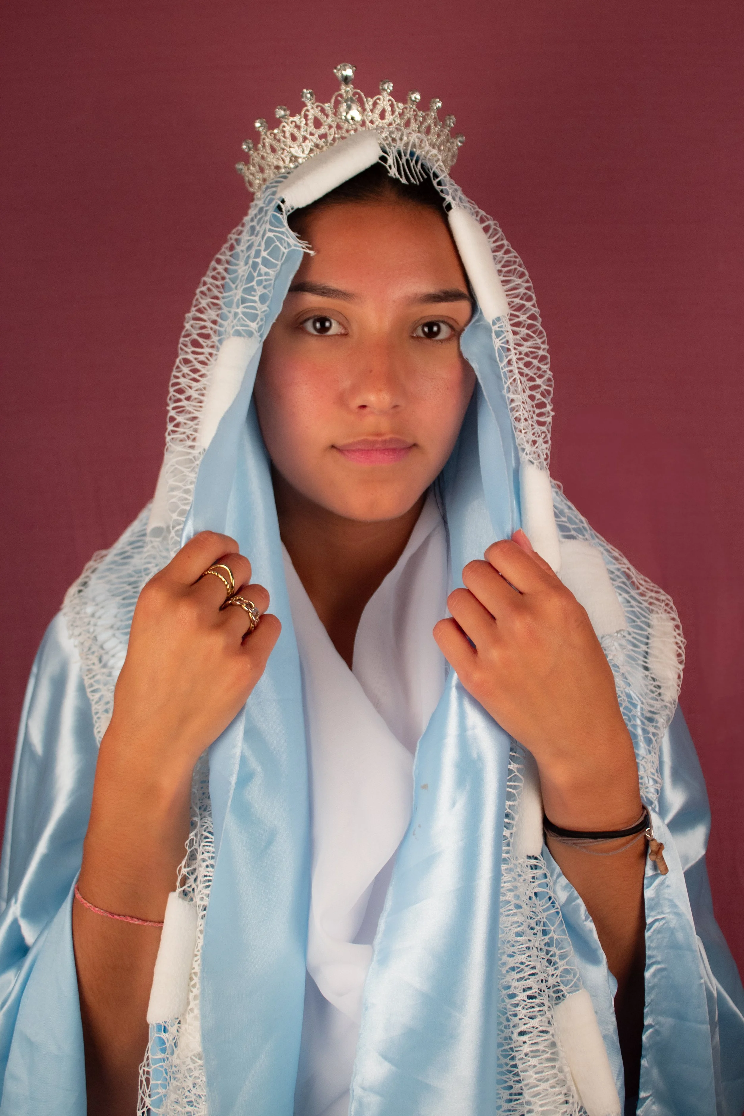 Jeune femme portant une couronne et une cape bleue, posant contre un fond rose