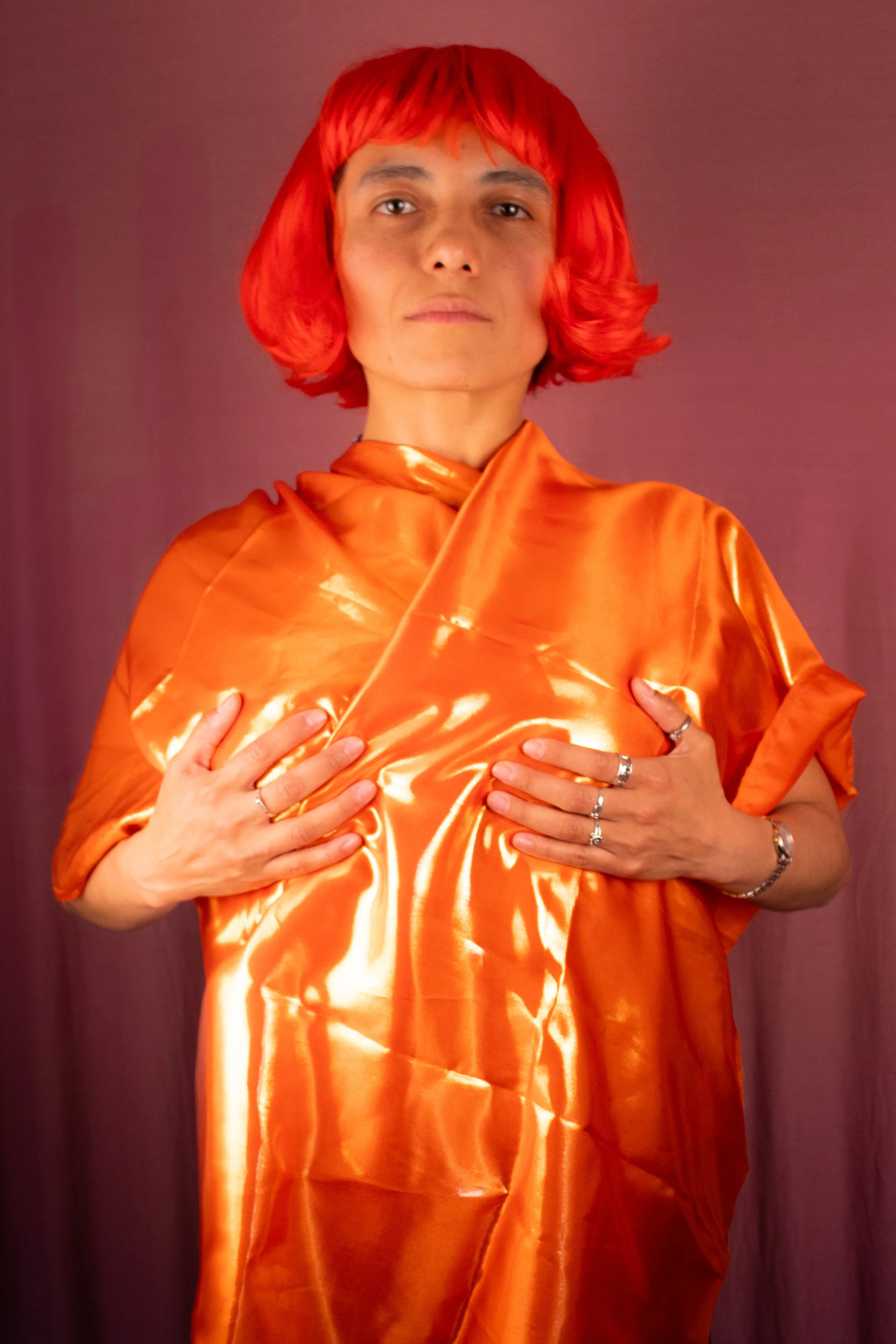 Personne portant une robe en satin orange avec une perruque rouge, tenant la robe avec ses mains.