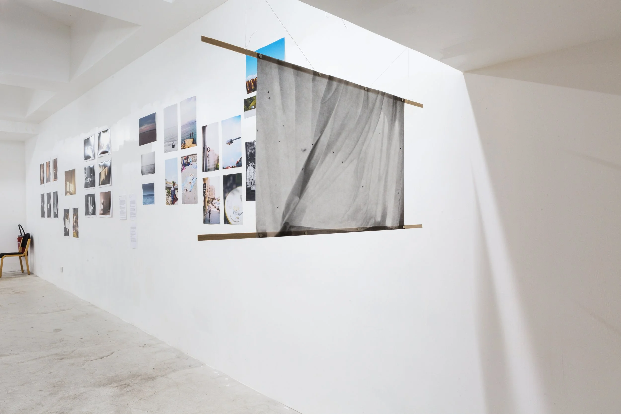 Exposition d'art avec plusieurs photographies affichées sur un mur blanc et un panneau en tissu gris suspendu.