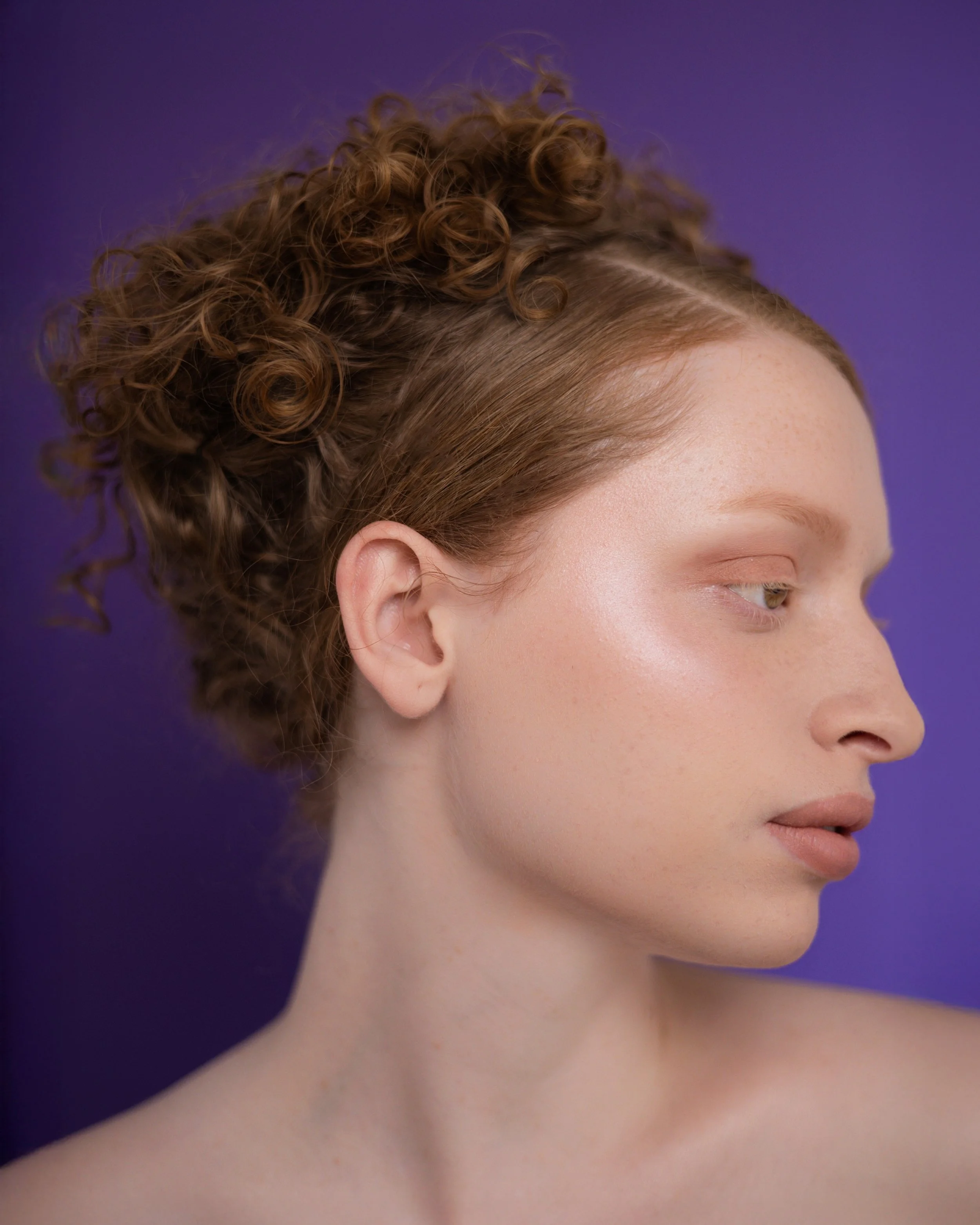 Shooting beauté. Profil d'une femme avec cheveux bouclés teints en roux, fond violet.