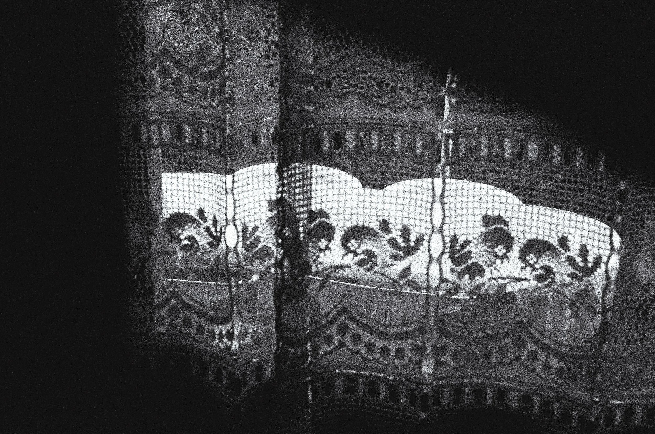 Une lampe avec un abat-jour en dentelle ou en broderie complexe, projetant un motif floral sur un mur ou une surface adjacente.