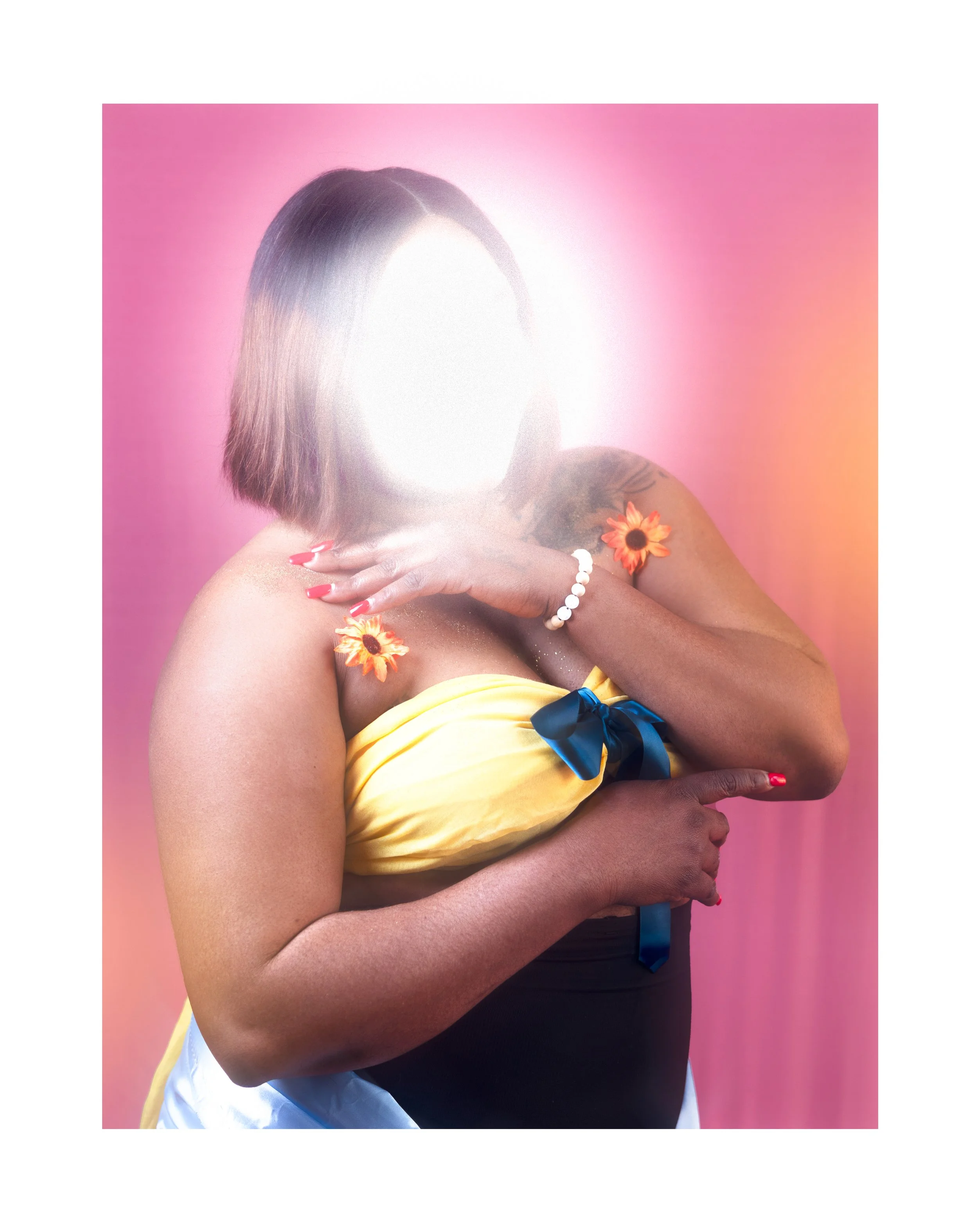 Une femme portant une robe jaune avec un nœud bleu, tenant ses épaules avec ses bras, contre un fond rose. Son visage est flouté par une forte lumière, et elle porte des fleurs sur ses épaules et un bracelet blanc.