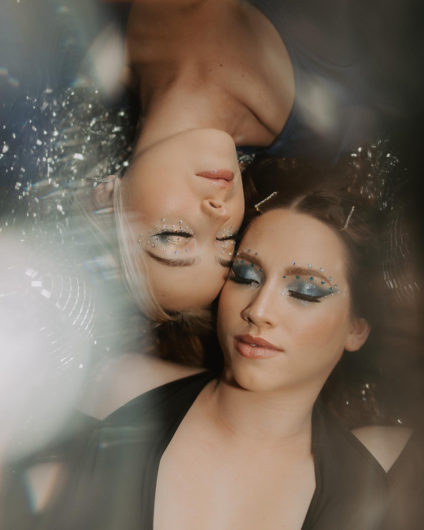 Two women adorned with metallic glitter makeup lying next to each other, with confetti and streamers around them
