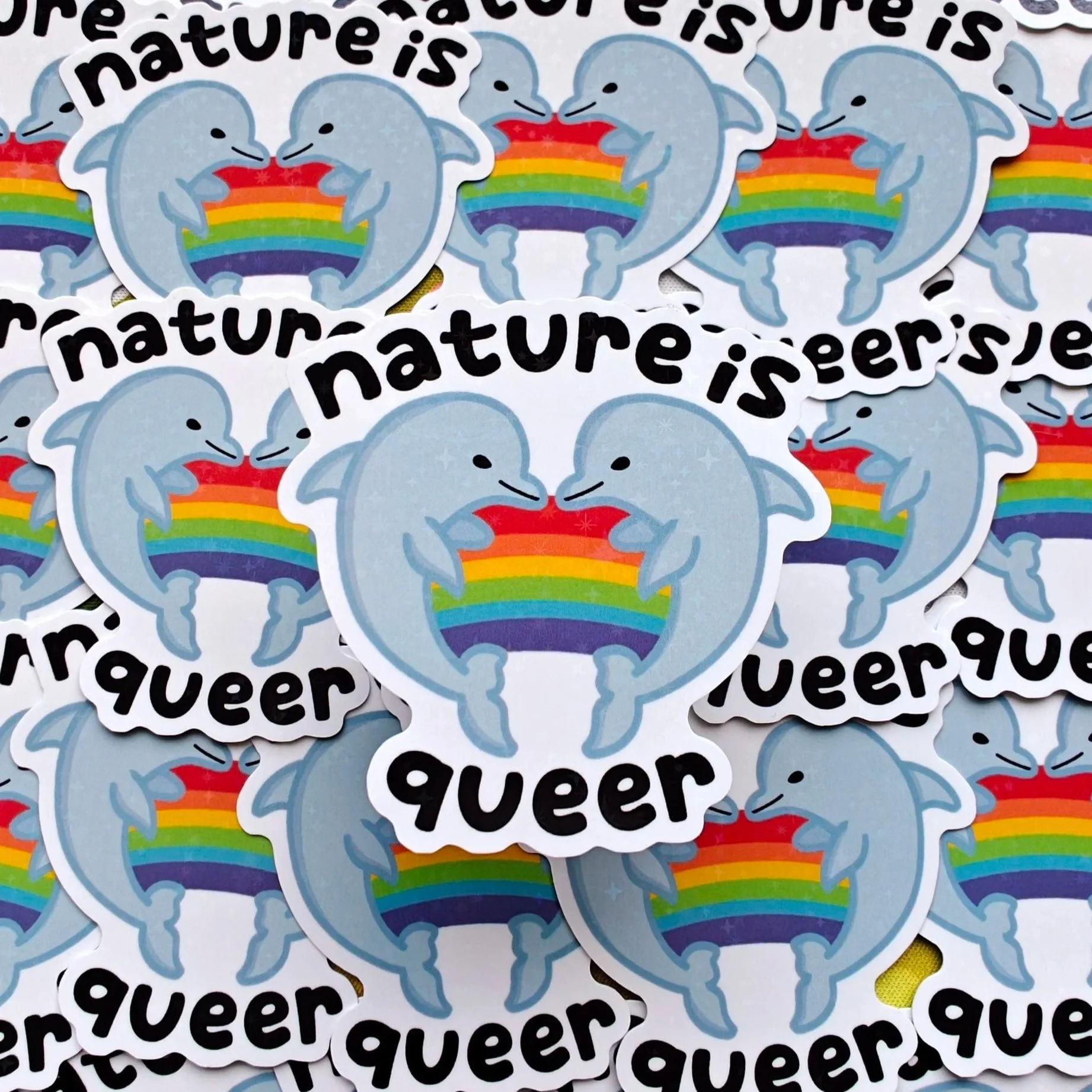 A collection of stickers featuring a light blue dolphin with a rainbow-shaped splash and the phrase "nature is queer" in black text.