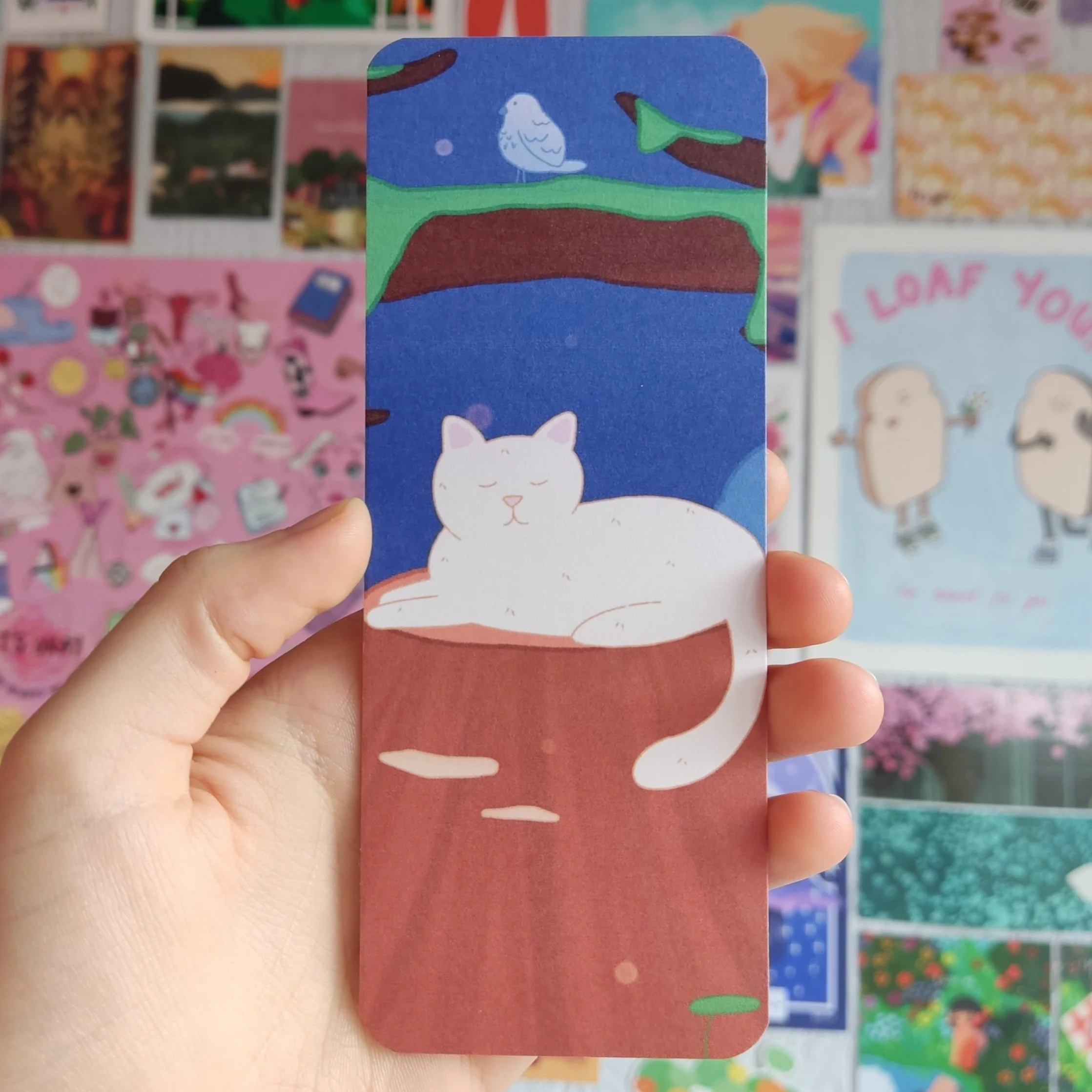 Illustration of a white cat relaxing in a cup, with a night sky, a bird, and trees in the background.