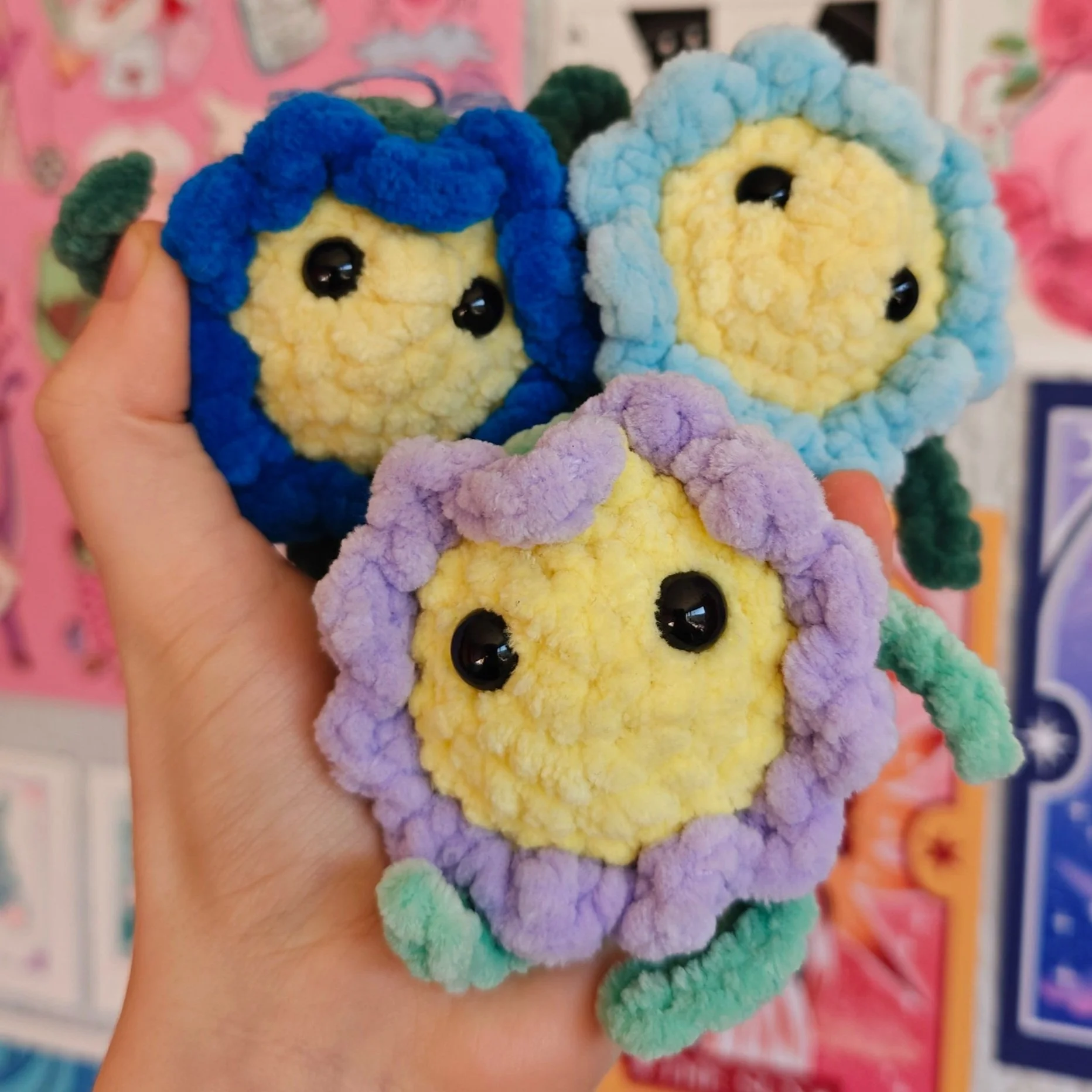 Colorful plush toys resembling flowers with cartoonish faces, held in a person's hand.