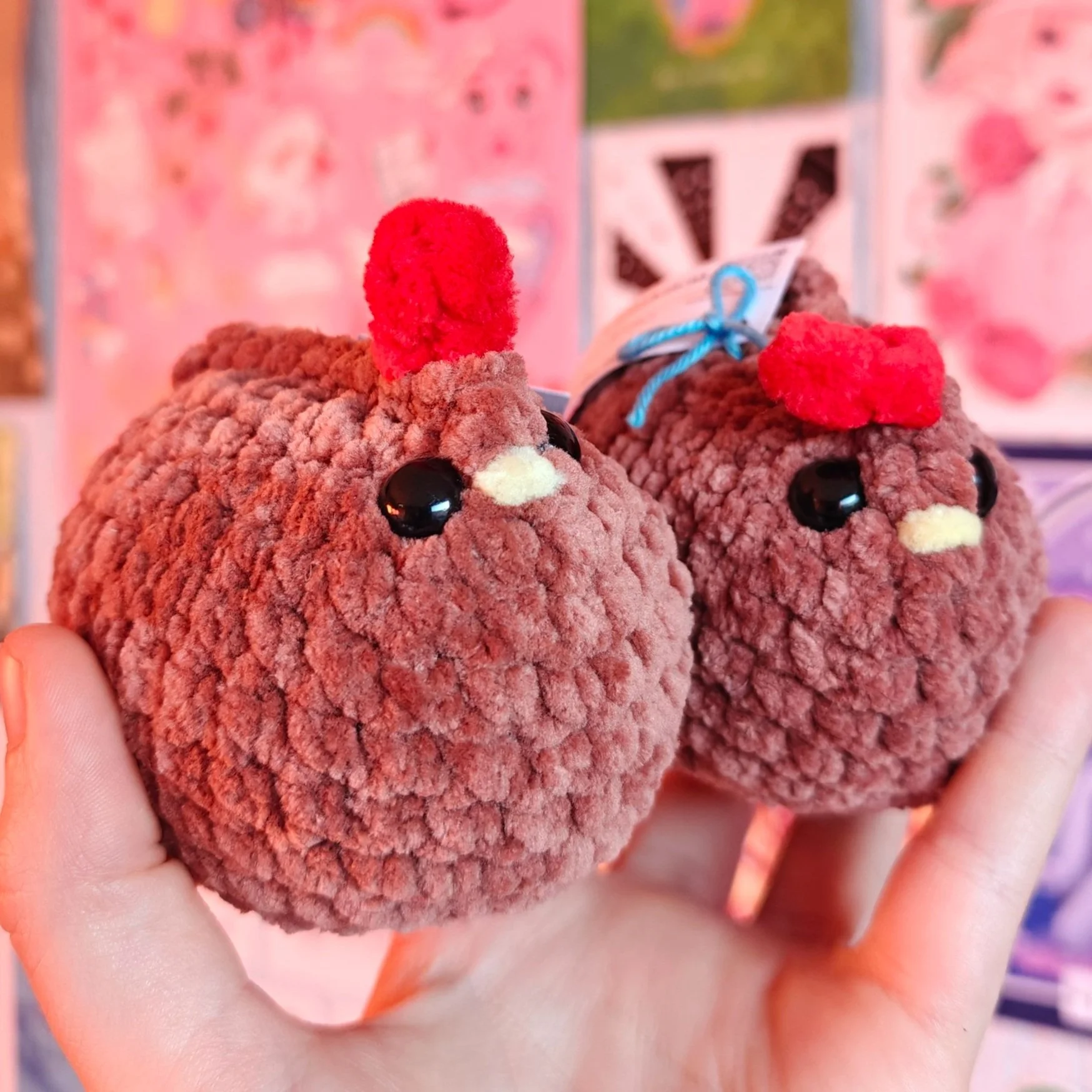 Two plush chicken-shaped plushies with red combs, black eyes, and small beak details, held in a person's hand.