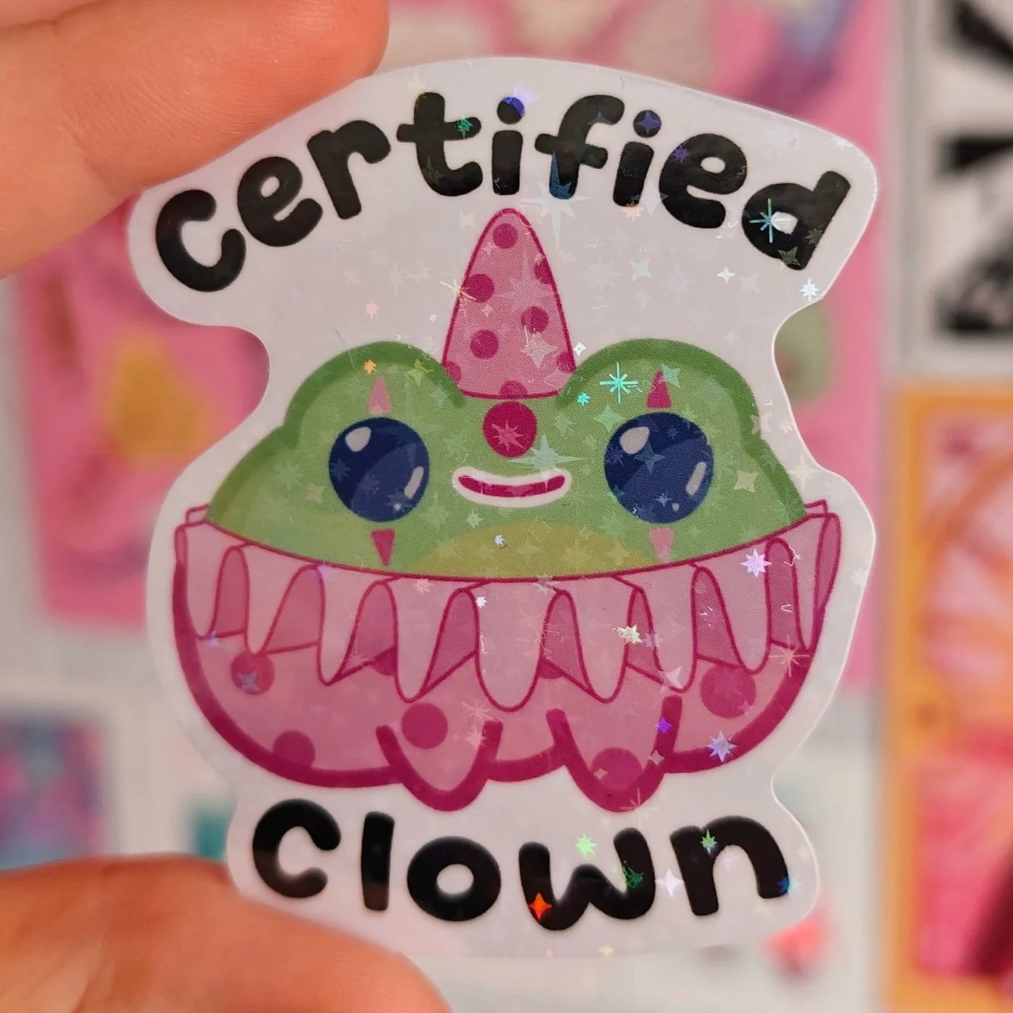 Sticker with a cute cartoon frog with a pink hat and a pink and purple shirt, and text that says 'certified clown'.
