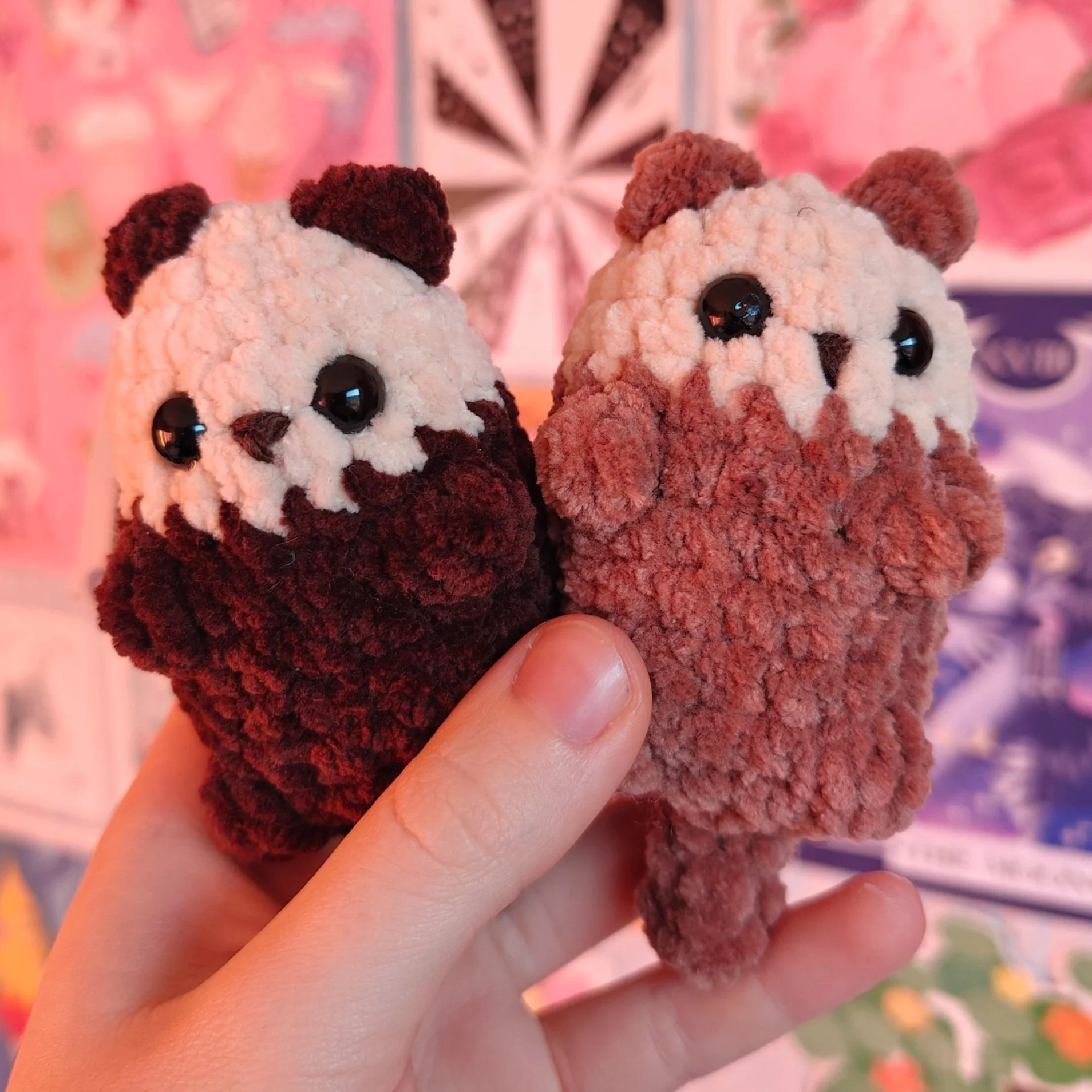 Two fuzzy plush toys resembling otter characters being held by a person. The toys have large black eyes and small noses, with one appearing darker and the other lighter in color.