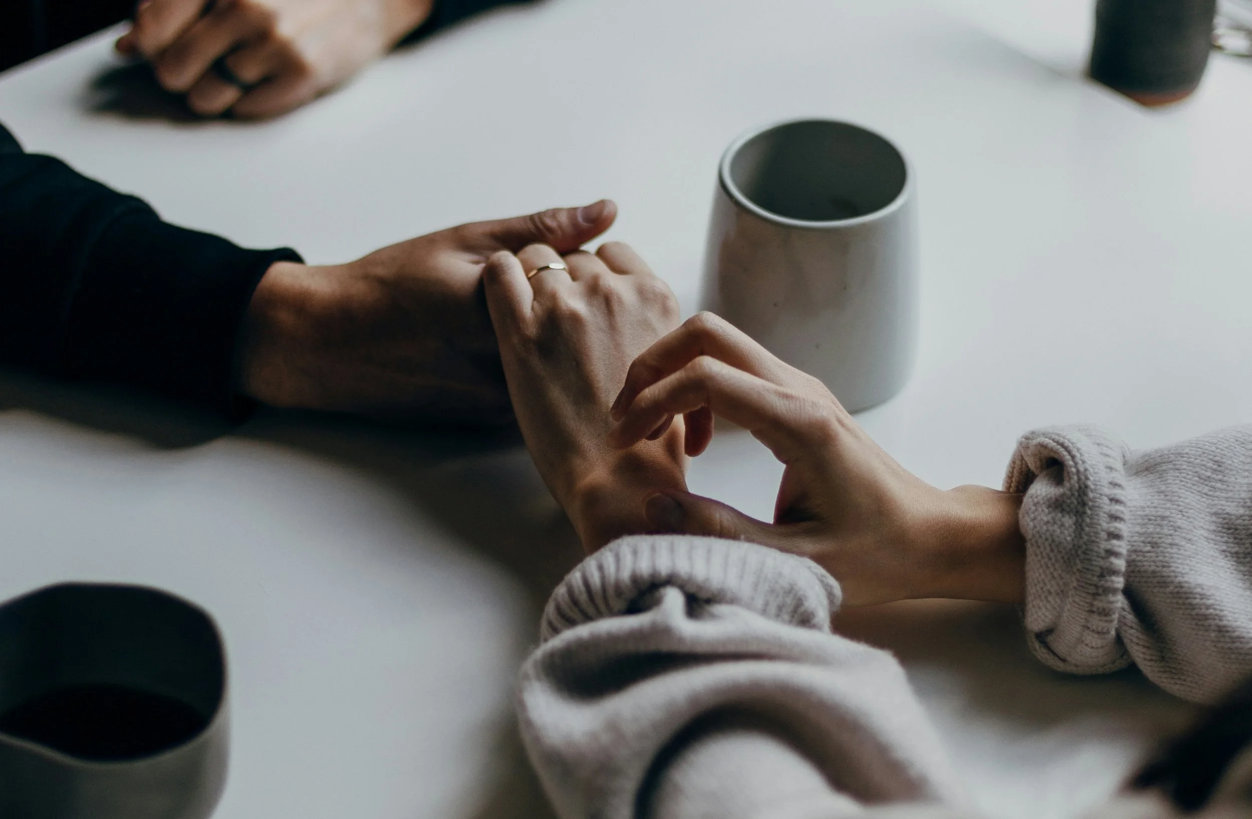 Two partners reaching for each other’s hands across a table, symbolizing emotional connection and trauma healing support when supporting a partner with trauma.